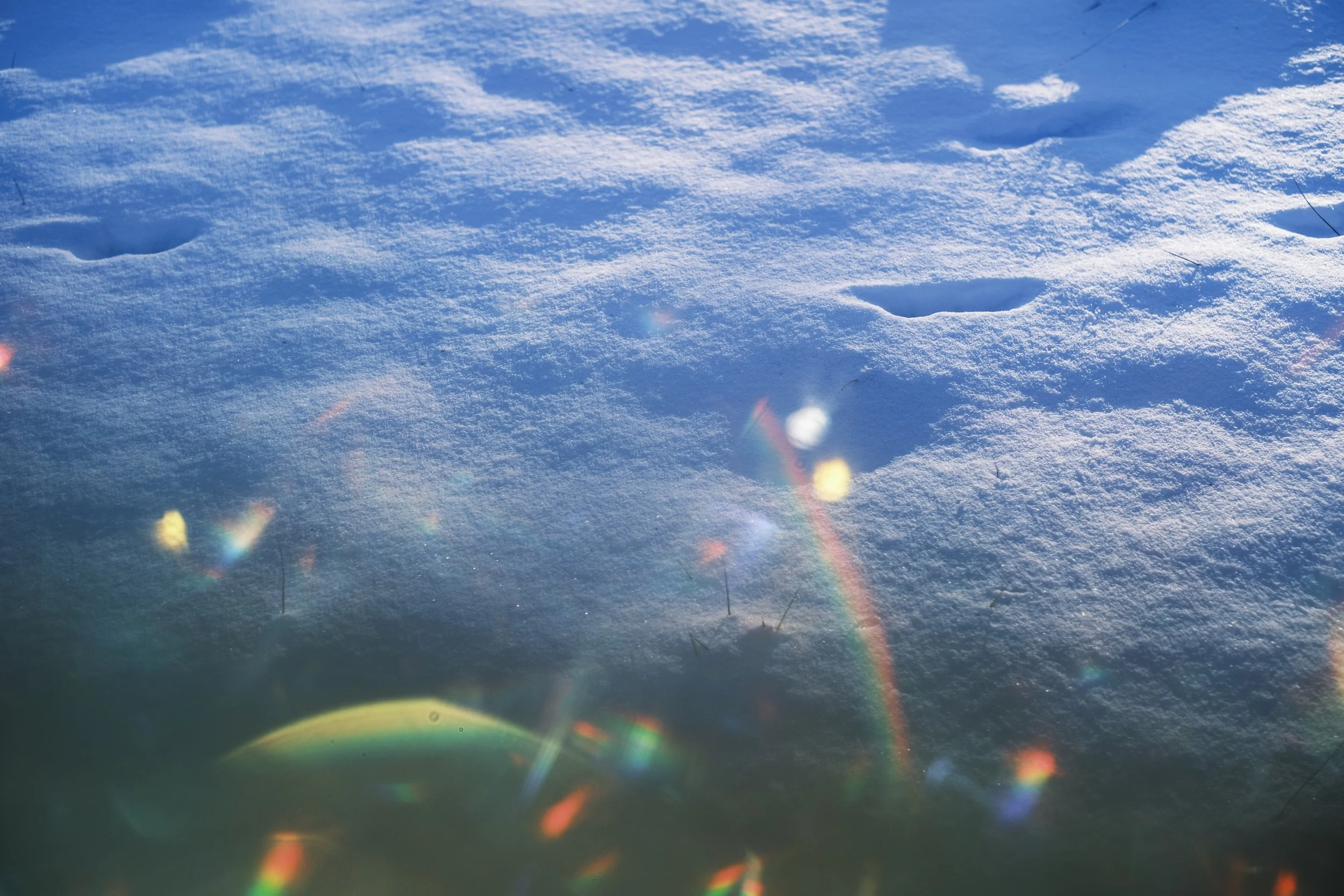 Freshly fallen snow with footprints and rainbow sun flares.