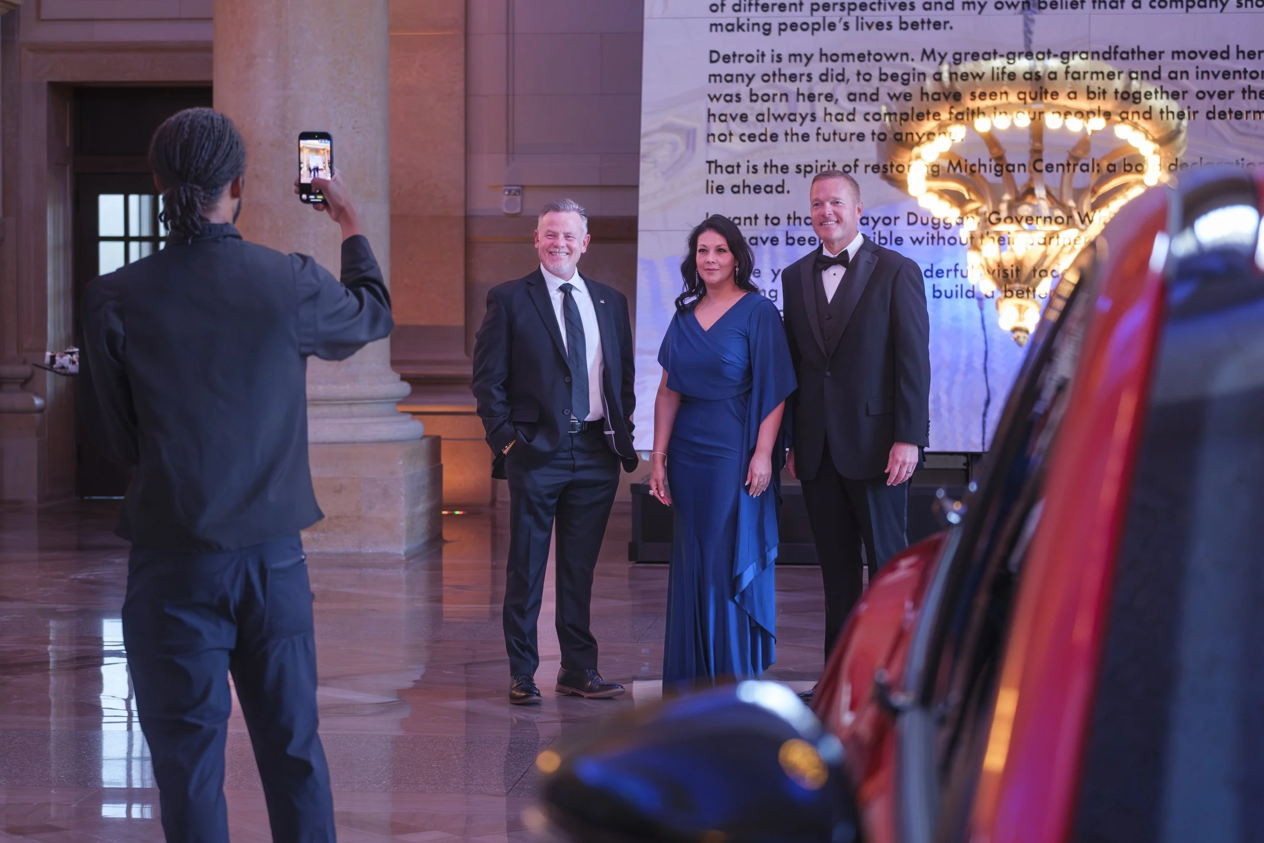 Three people stand while posing for a cell phone photo being taken by a caterer at the Ford Supplier Summit Awards at Michigan Central Station.