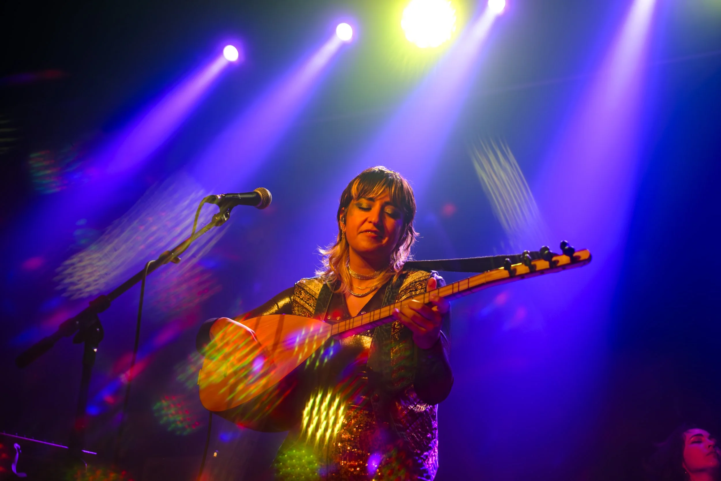 Derya Yildirim and Grup Simsek perform while Derya looks down at her Turkish Lute, with stage lighting in the background on stage during their concert at The Magic Bag in Ferndale, Michigan.
