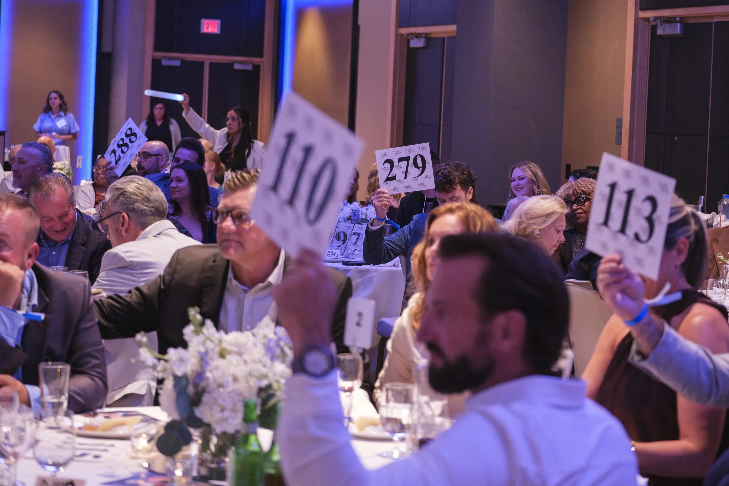 A crowd of people hold up their paddles with various three digit numbers, pledging money to raise funds for the Jamie Daniels Foundation.