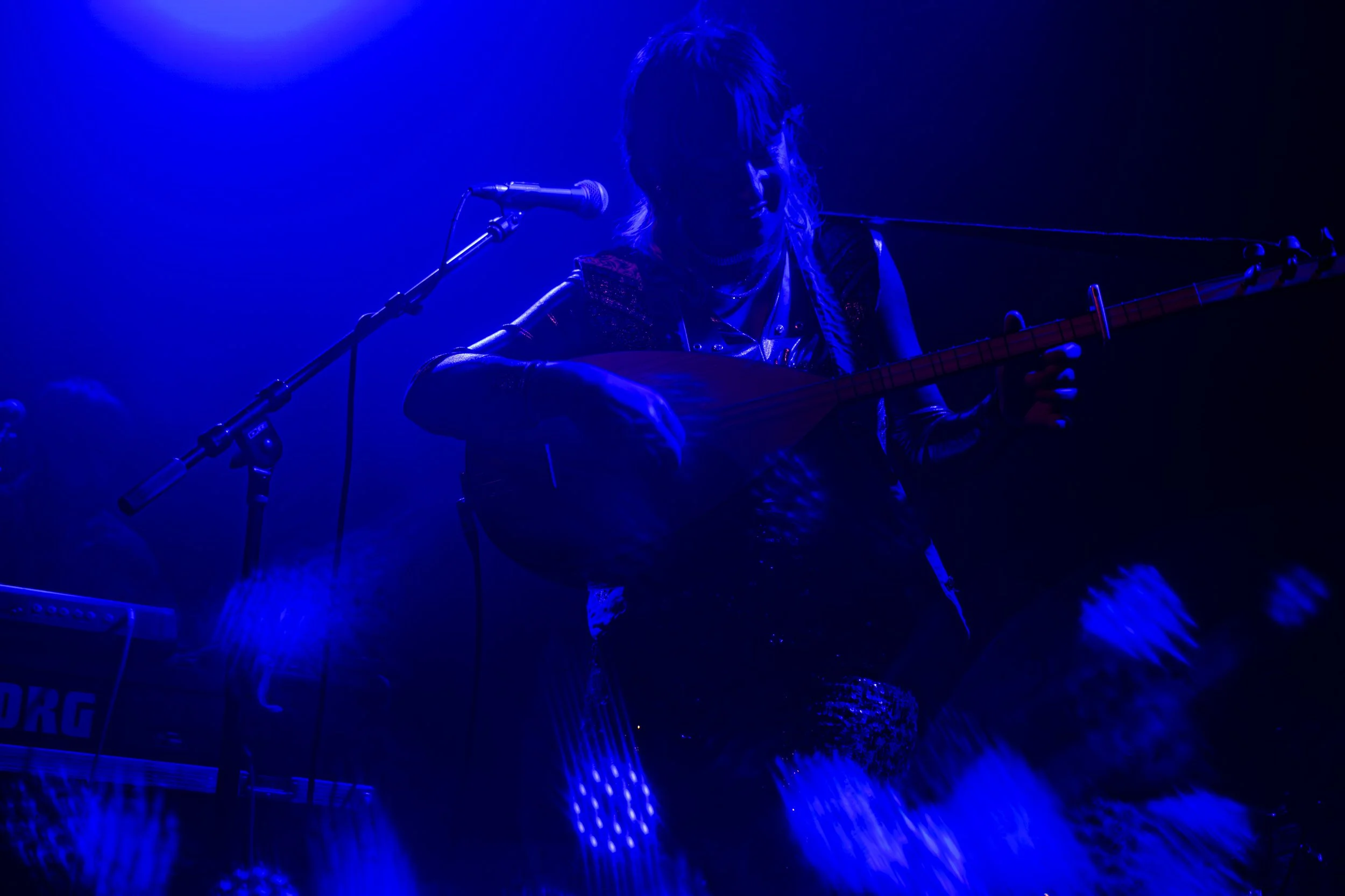Singer Derya Yildirim of Derya Yildirim and Grup Simsek plays the turkish lute on stage during a concert in ferndale michigan, surrounded by blue stage lighting.
