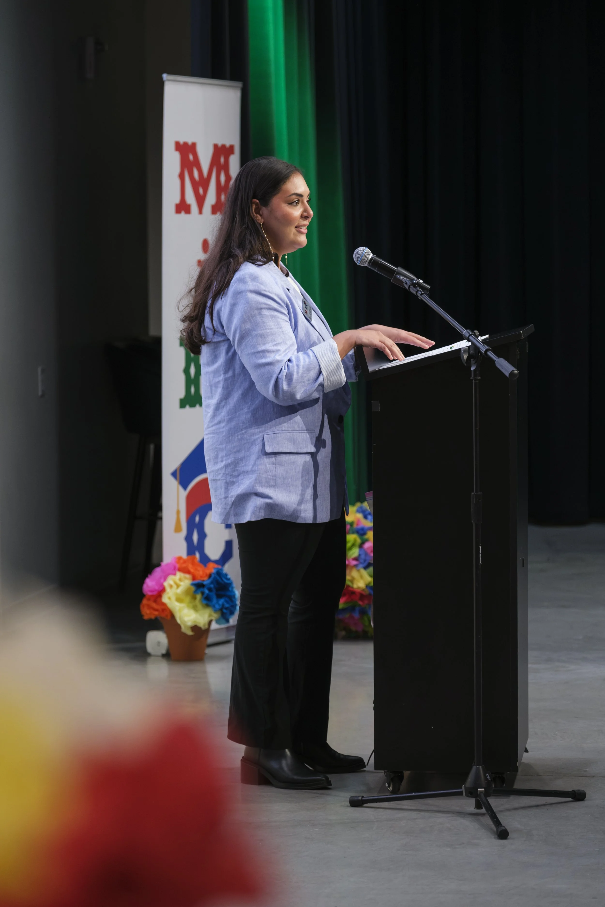A young woman wearing a blazer speaks into a microphone behind a podium.