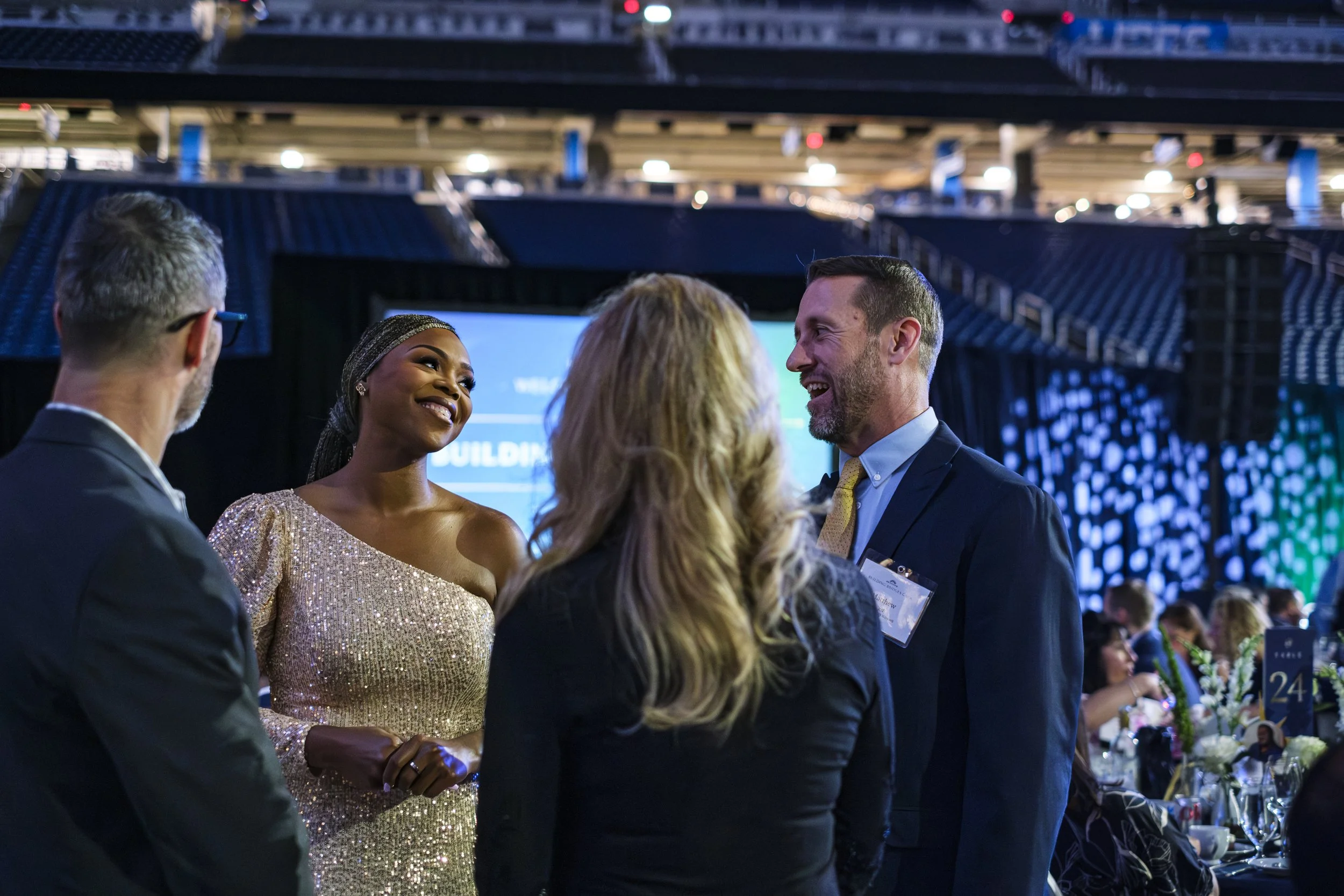 A woman wearing a sequin gowns smiles while a man talks to her during the non profit Pope Francis Center Building Bridges Gala at Ford Field.