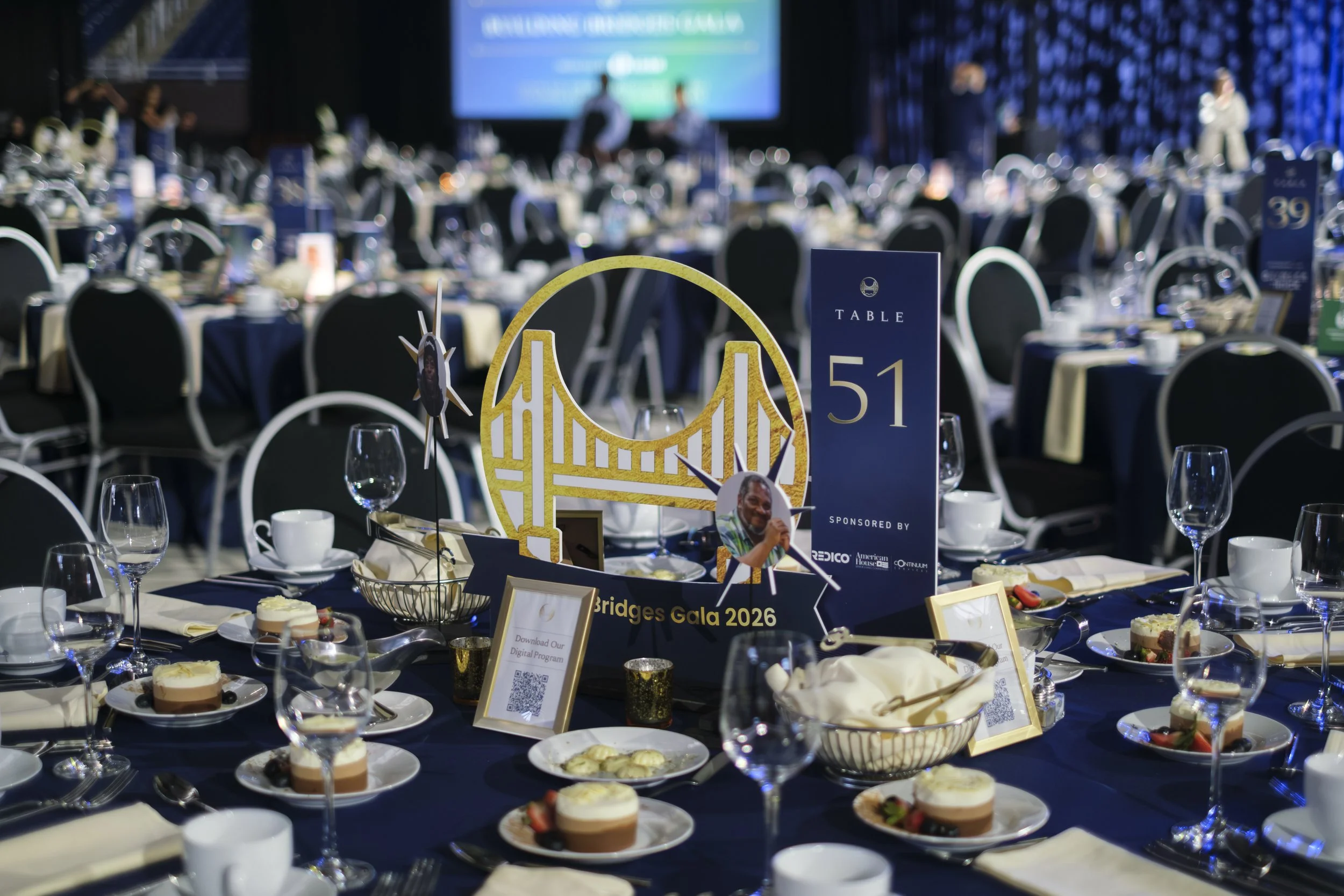 An elaborate table setting with plates, wine glasses and a with a centerpiece that reads "Table 51 Building Bridges Gala"