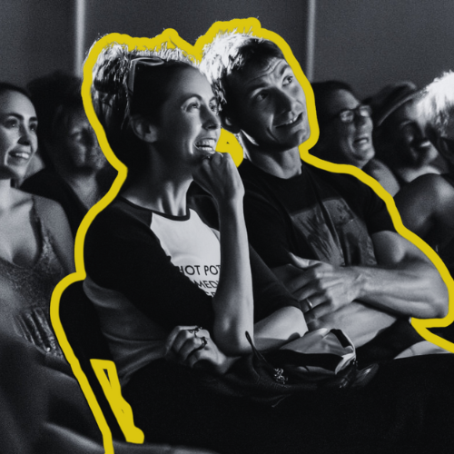 People watching a comedy show, with one woman smiling and a man looking amused.