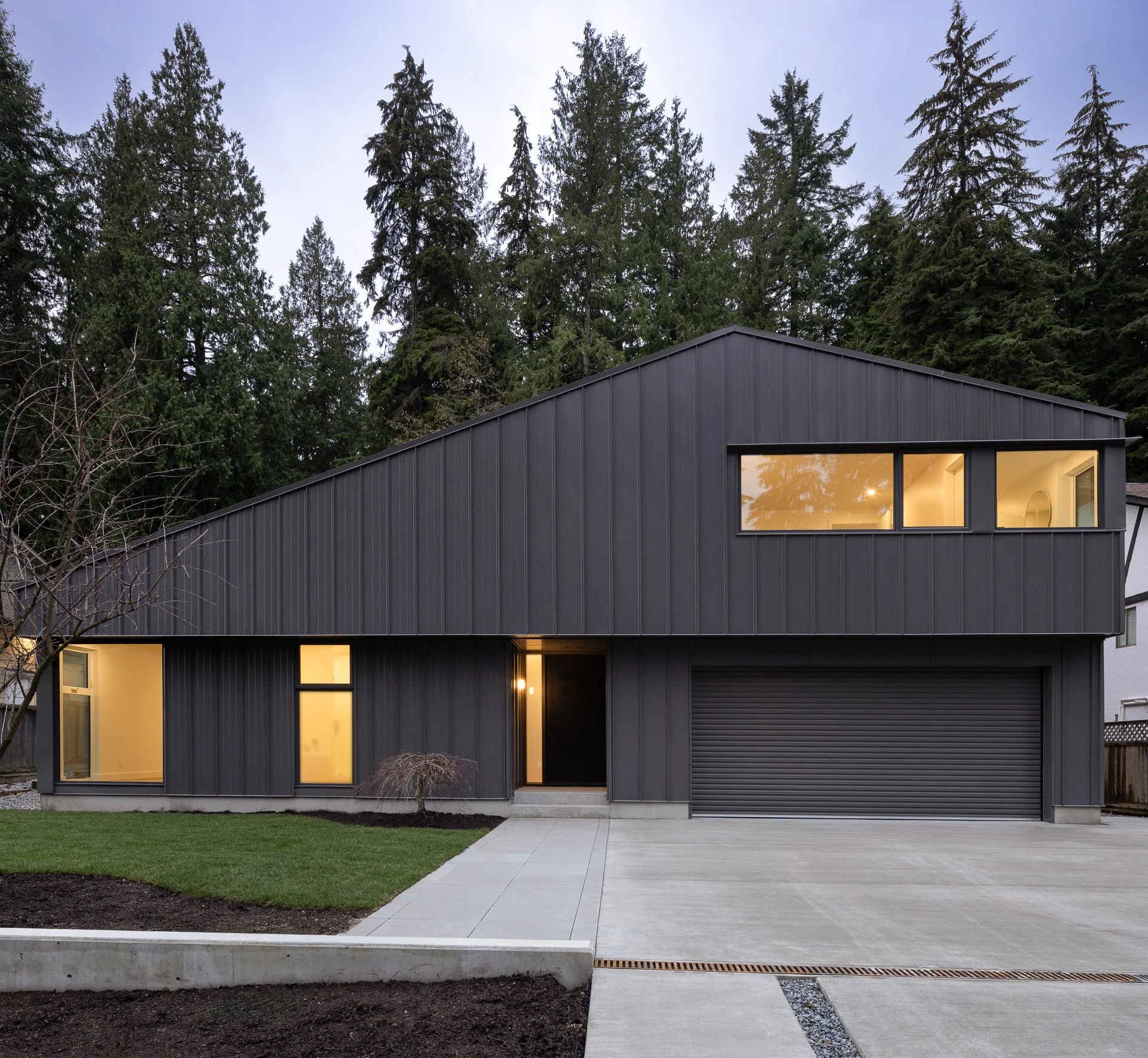 Skyline House | Modern black two-story house in North Vancouver with large windows and attached garage, surrounded by trees and a concrete driveway.