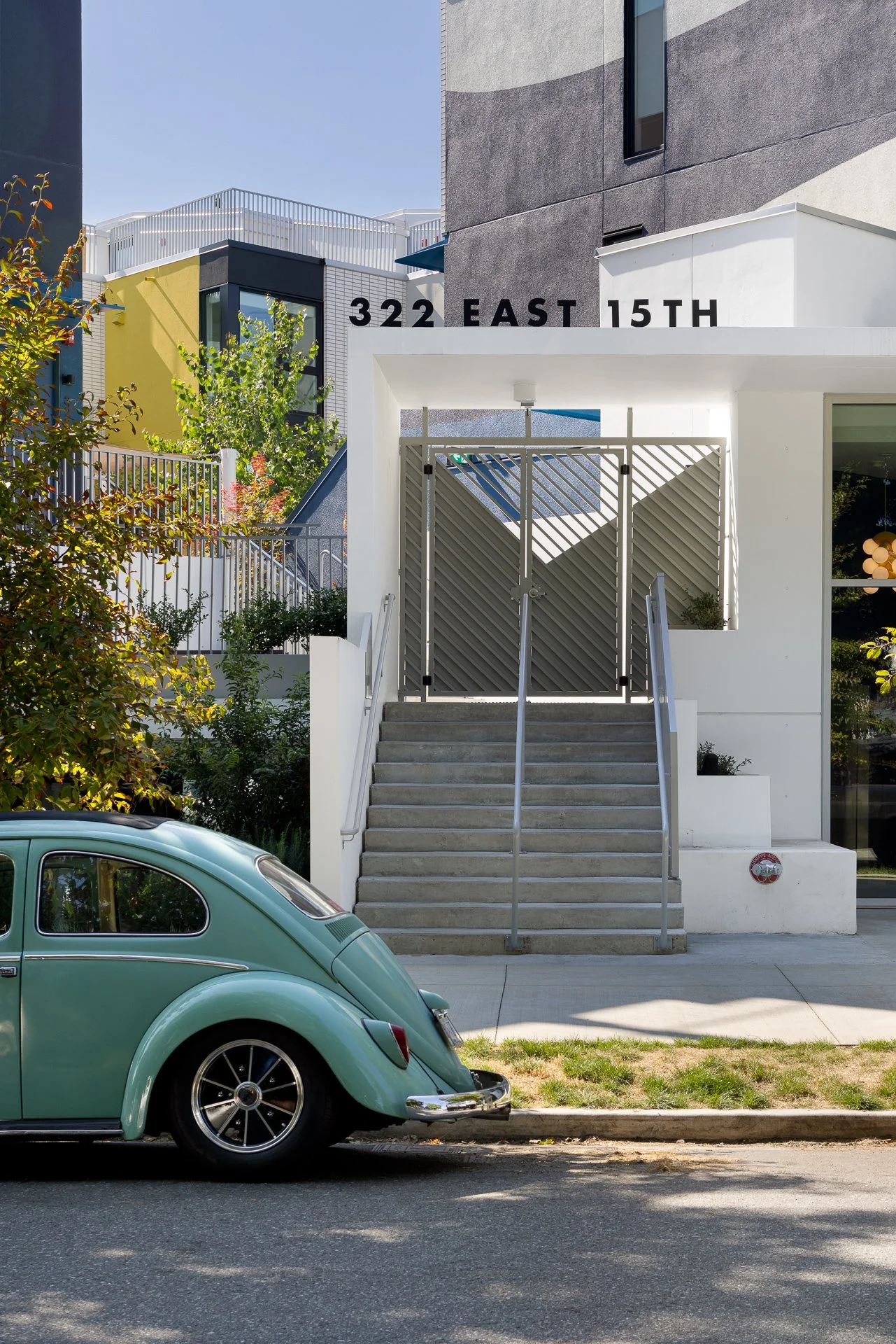 A vintage green Volkswagen Beetle parked in front East 15th townhomes in Vancouver, BC