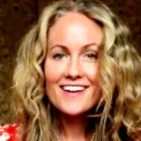 Close-up of a woman with curly blonde hair smiling at the camera.