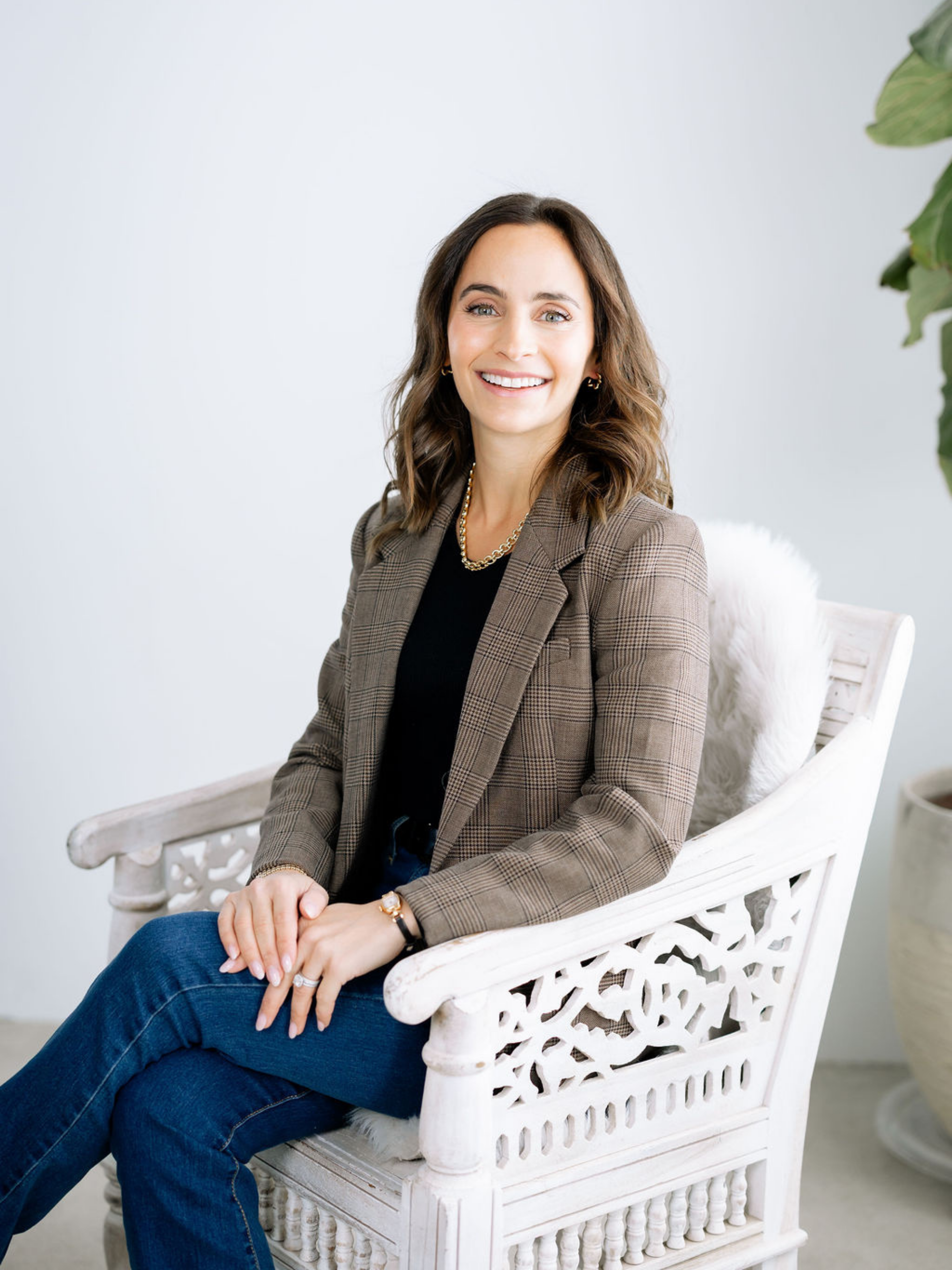 A brunette woman smiing at the camera while sitting in a white chair
