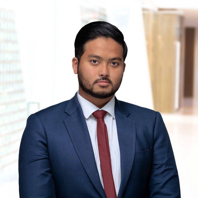 Professional man in a navy suit and red tie standing indoors with bookshelves in the background.