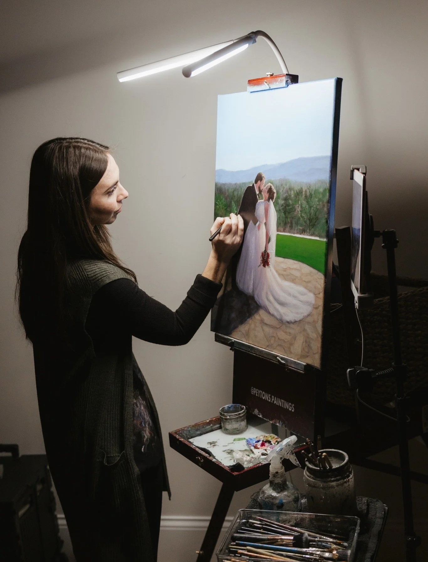 A live event painter painting a wedding scene on a canvas, depicting a bride and groom outdoors.