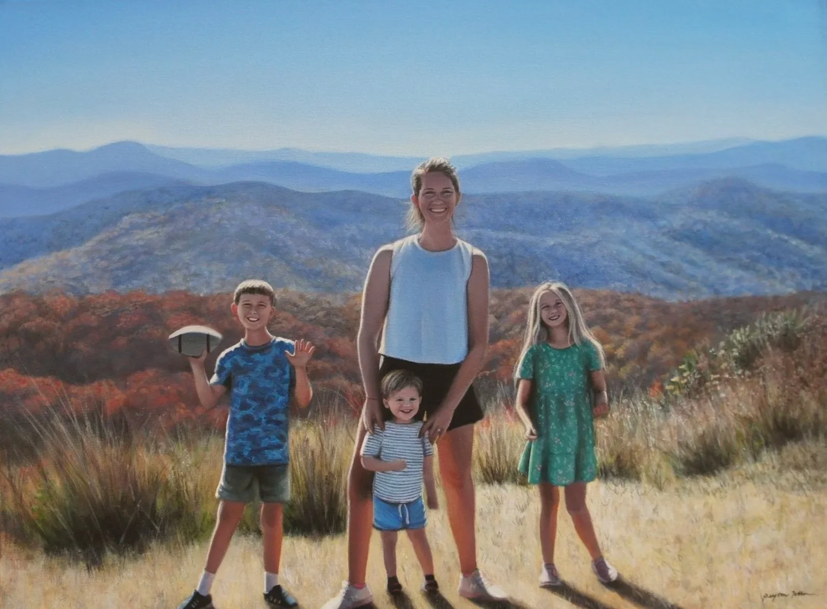 A woman and three children standing outdoors on a hillside with a mountain range in the background. The woman is smiling and wearing a white sleeveless top and black shorts. The children are smiling; one boy on the left is holding a frisbee, the girl on the right is in a green dress, and the youngest girl in the middle is in a striped shirt and blue shorts.