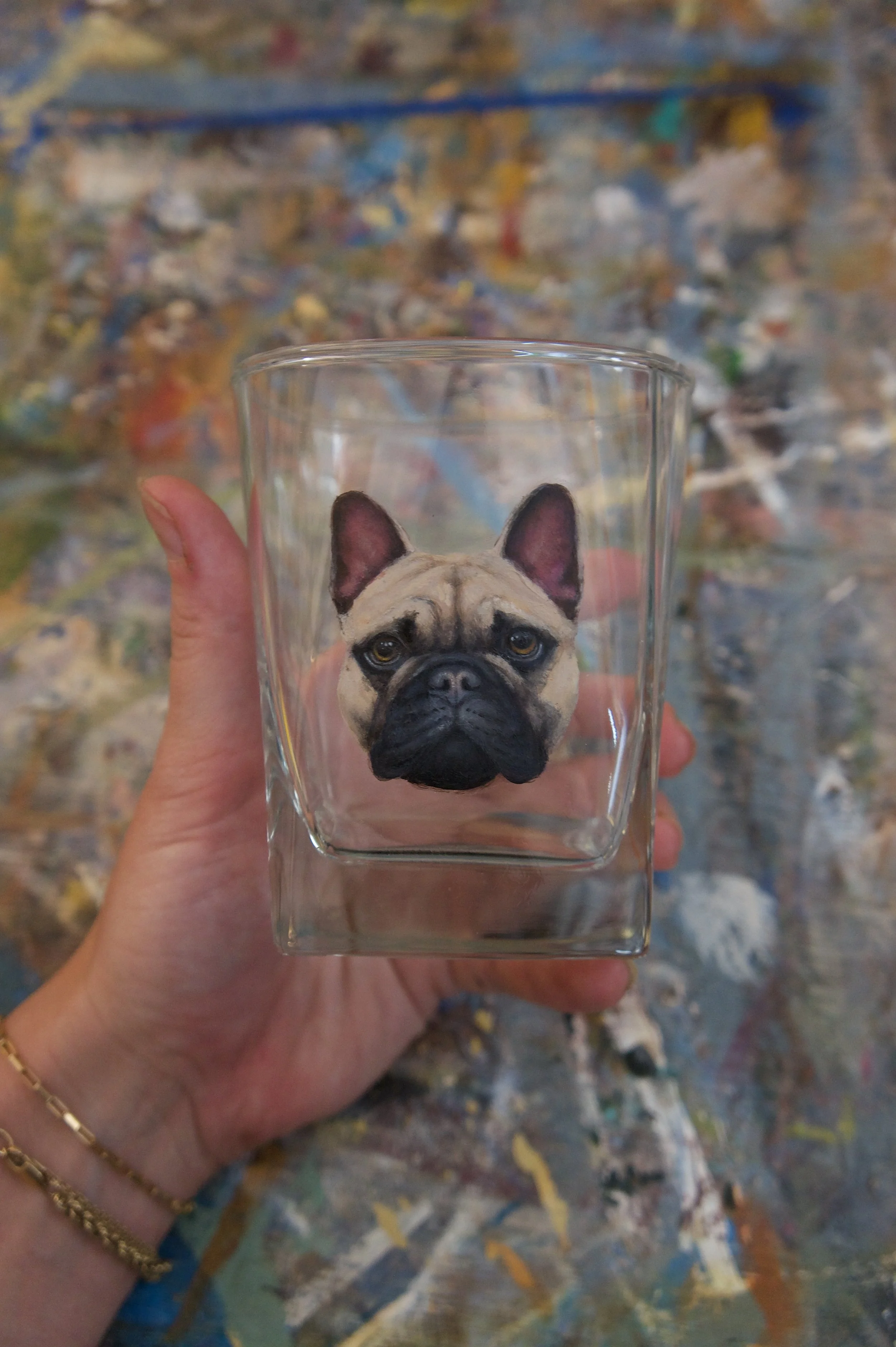 A hand holding a glass container with a detailed 3D portrait of a French Bulldog's face attached to the front.
