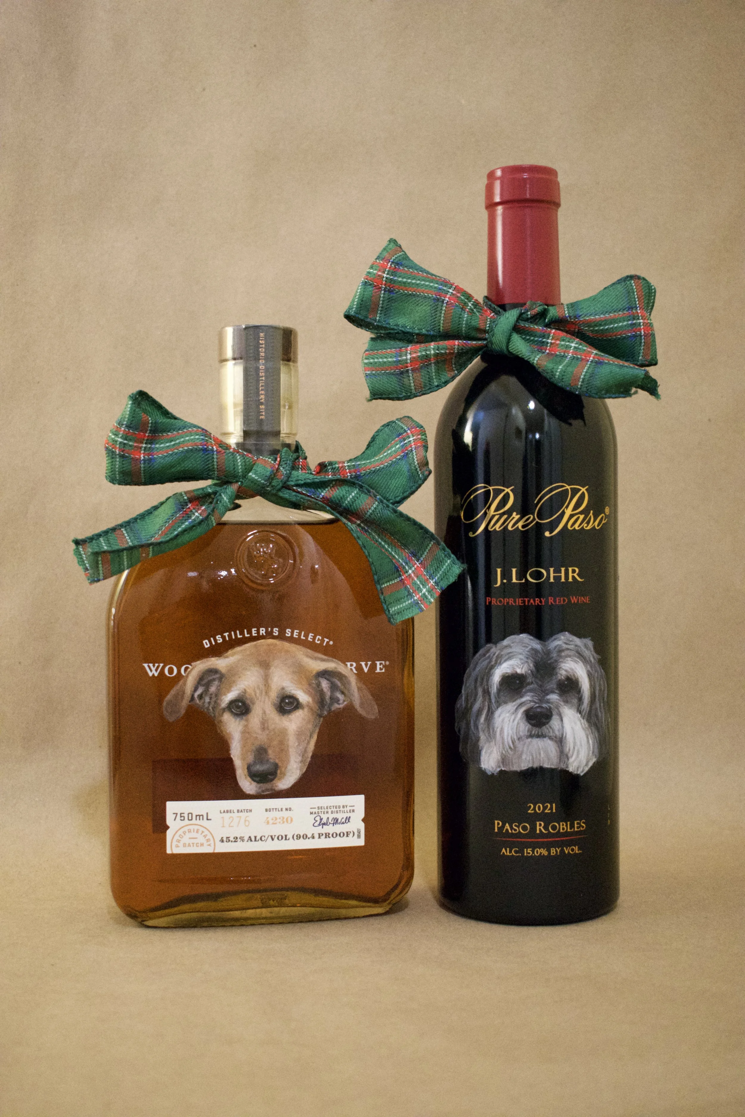 Two bottles of alcohol with dog-themed labels and green plaid ribbons tied around their necks, set against a plain background.