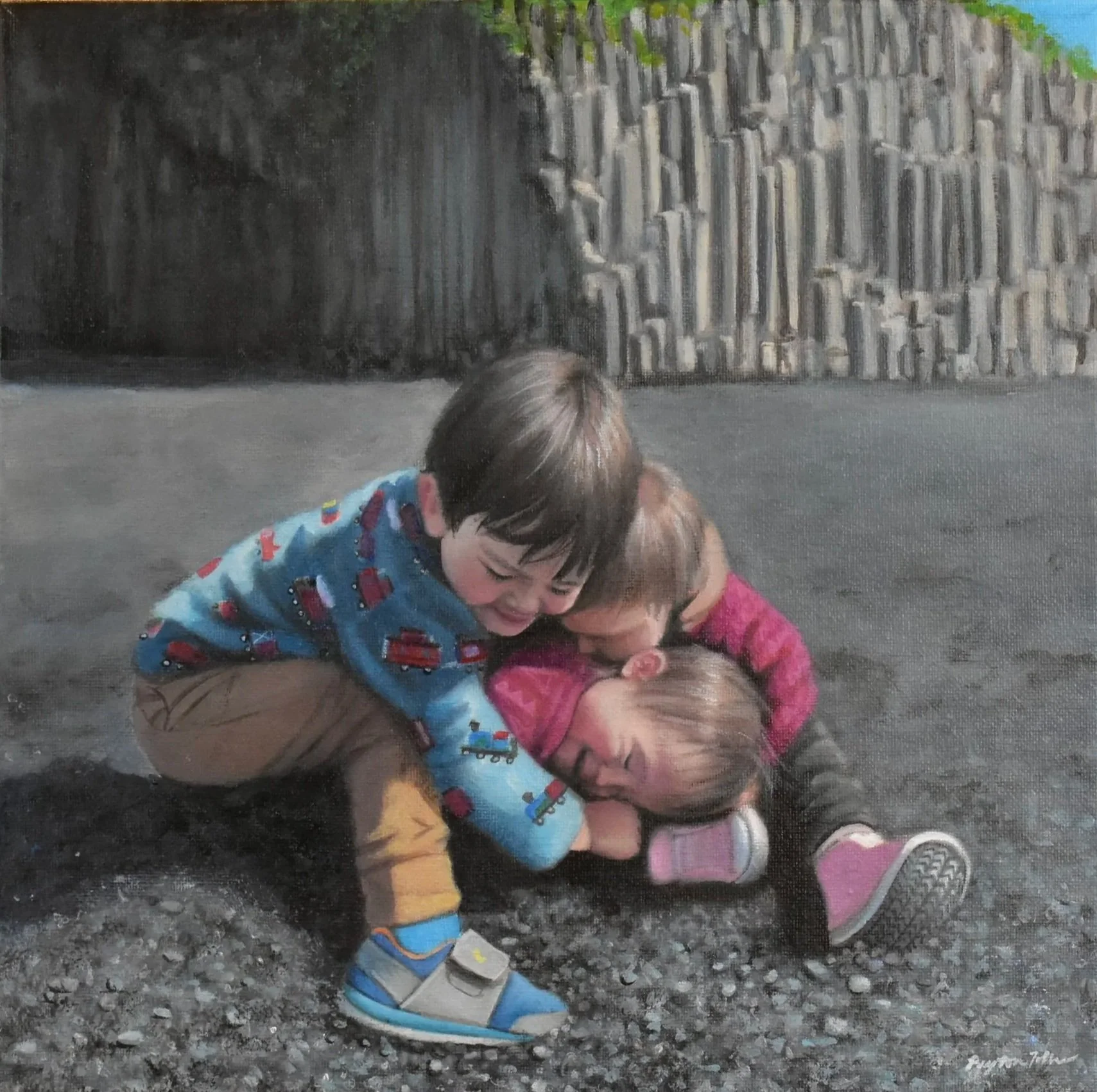 Three young children playing and laughing together on the ground outdoors near a tall wooden fence.