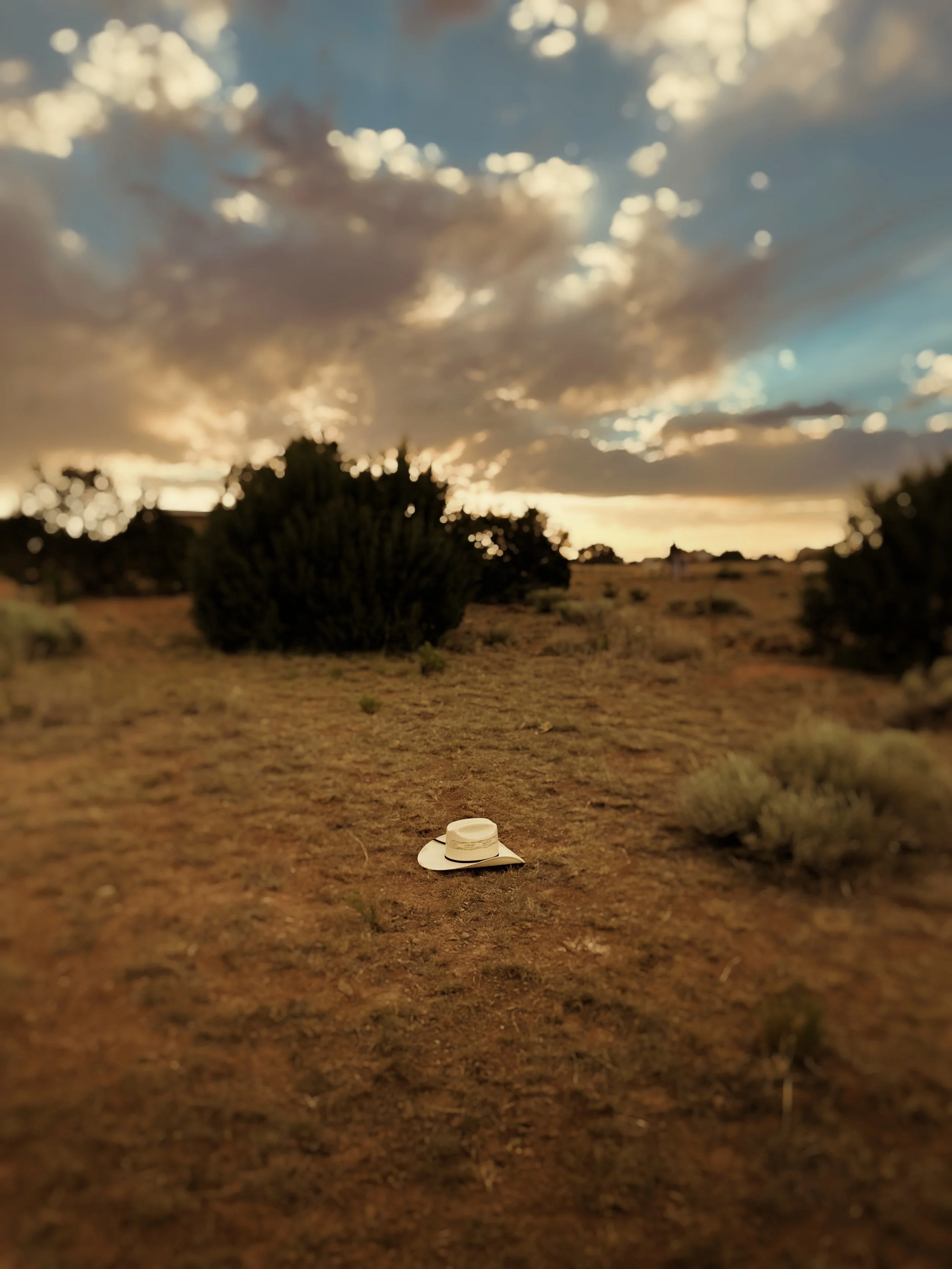 A wide open desert landscape at sunset with clouds in the sky and a white hat lying on the ground in the foreground.