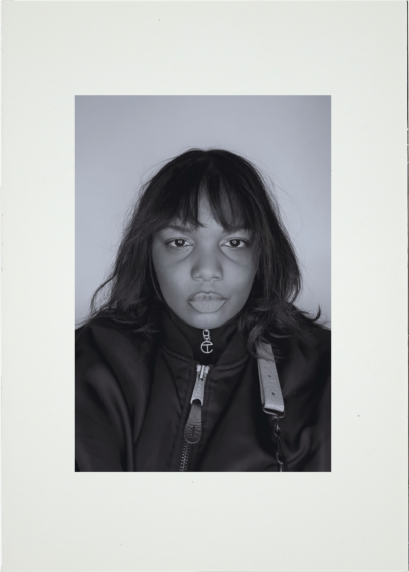 Black and white photo of a woman with shoulder-length hair wearing a zip-up jacket, looking directly at the camera with a neutral expression.