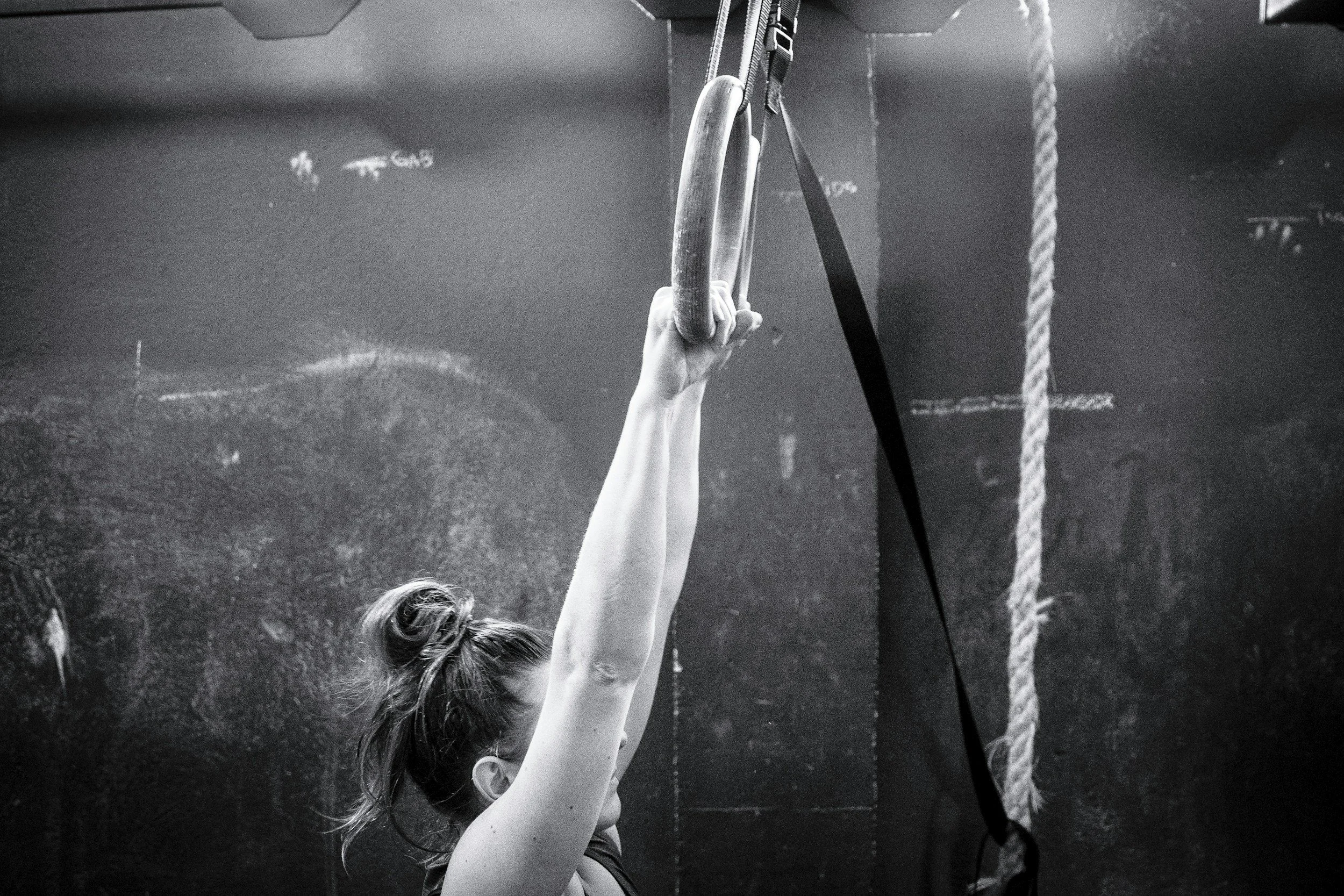 A woman exercising at a gym, holding onto gymnastic rings.