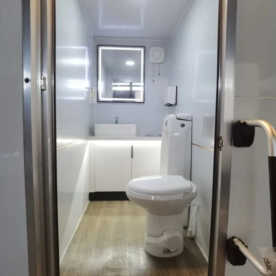 Small, white bathroom with a toilet, sink, mirror, and a window, viewed through a doorway.