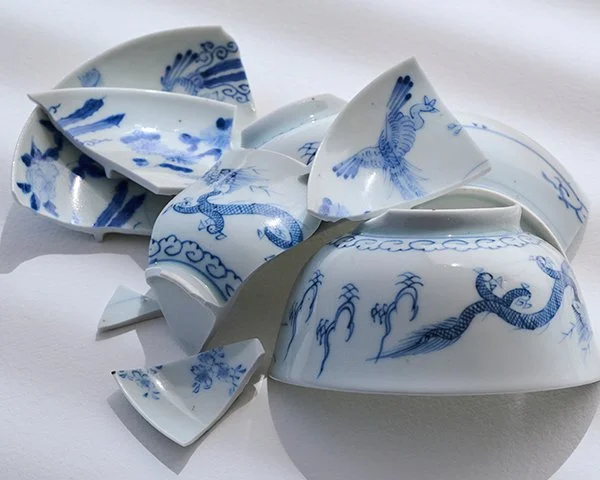Several pieces of a broken white ceramic bowl decorated with intricate blue dragon and phoenix patterns, arranged on a white background.
