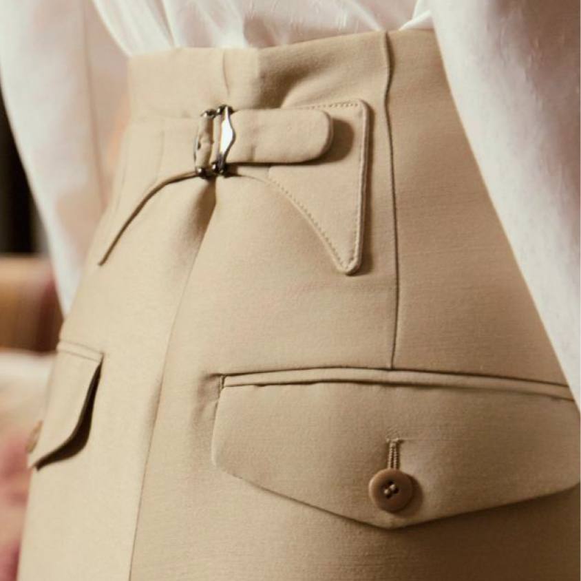 BIA LUCINA. womenswear  Close-up of beige high-waisted pants with belt, zipper, and pocket details.