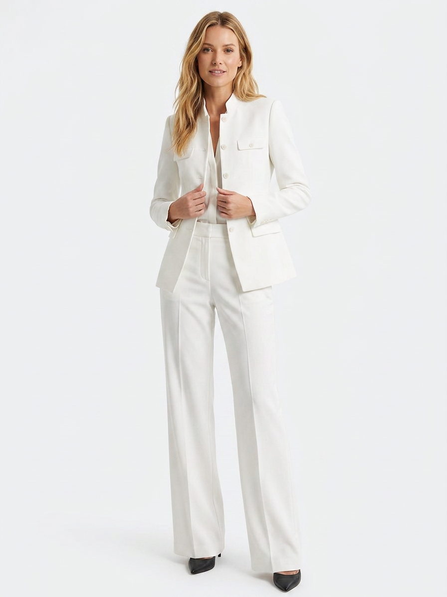 A woman in an all-white pantsuit, standing with her hands touching her jacket, against a plain white background.