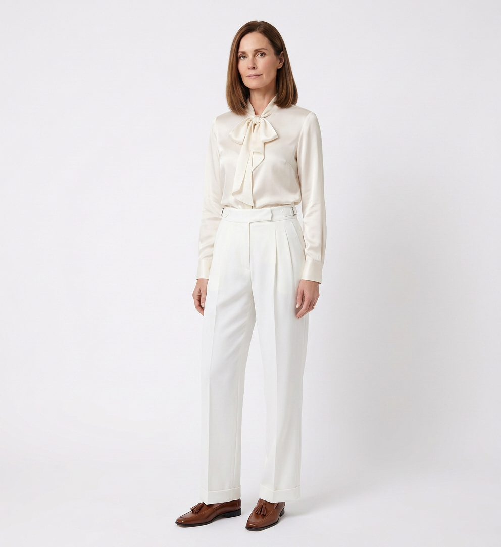Woman in elegant white outfit with blouse and high-waisted trousers standing against a plain white background.