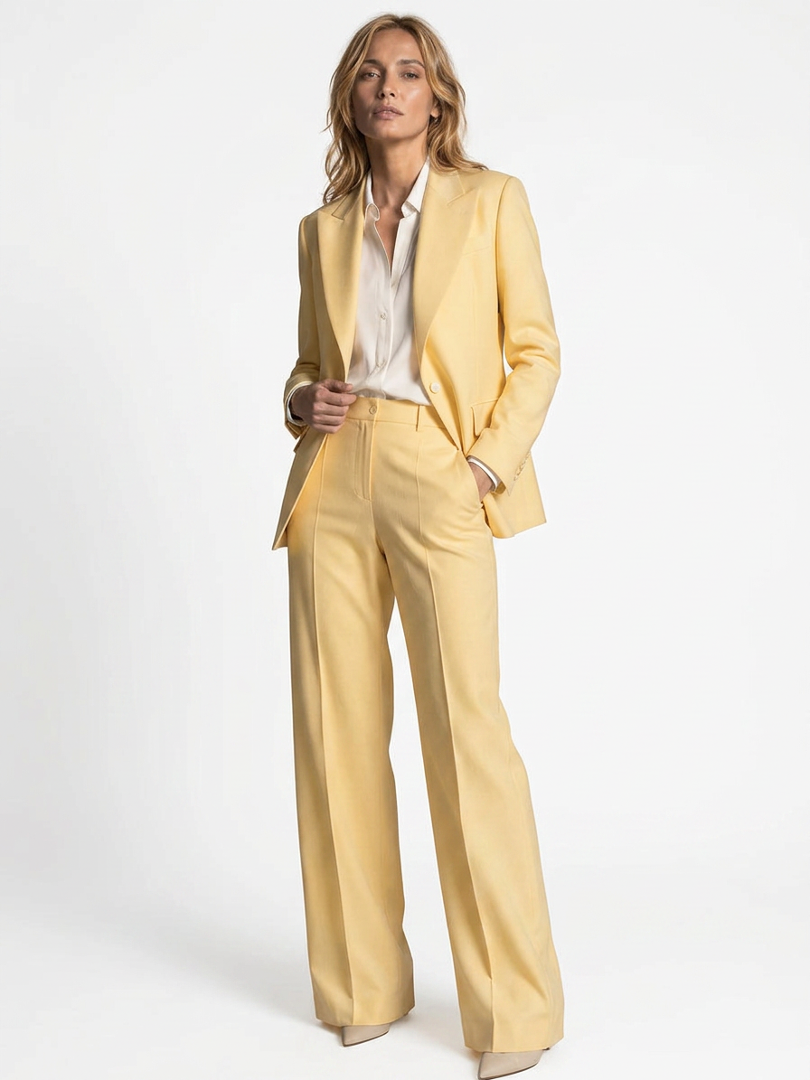 A woman in a yellow suit, including a blazer and wide-leg trousers, with a white shirt, standing against a plain white background.