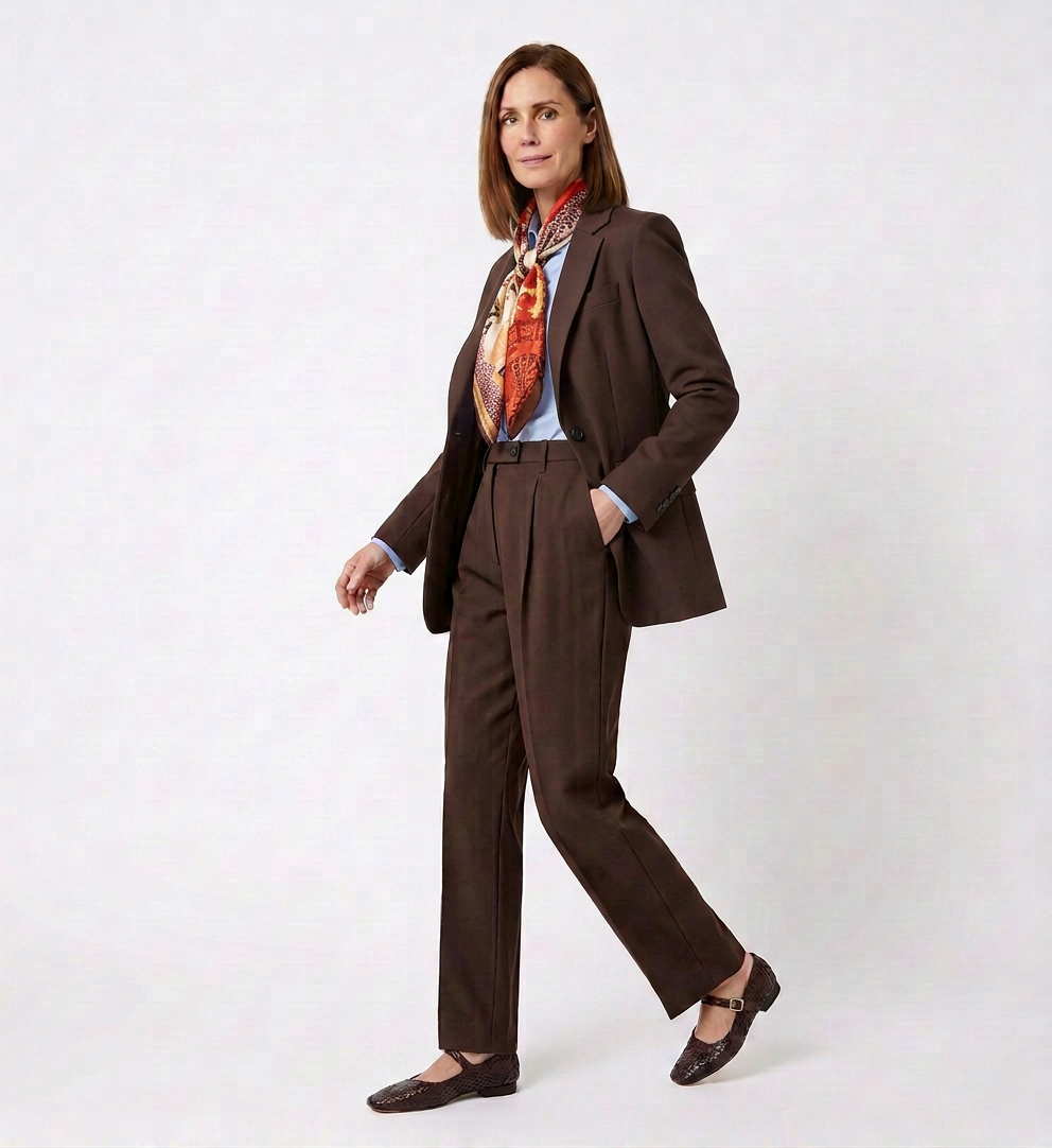 A woman wearing a brown pantsuit with a colorful scarf, standing against a plain white background.