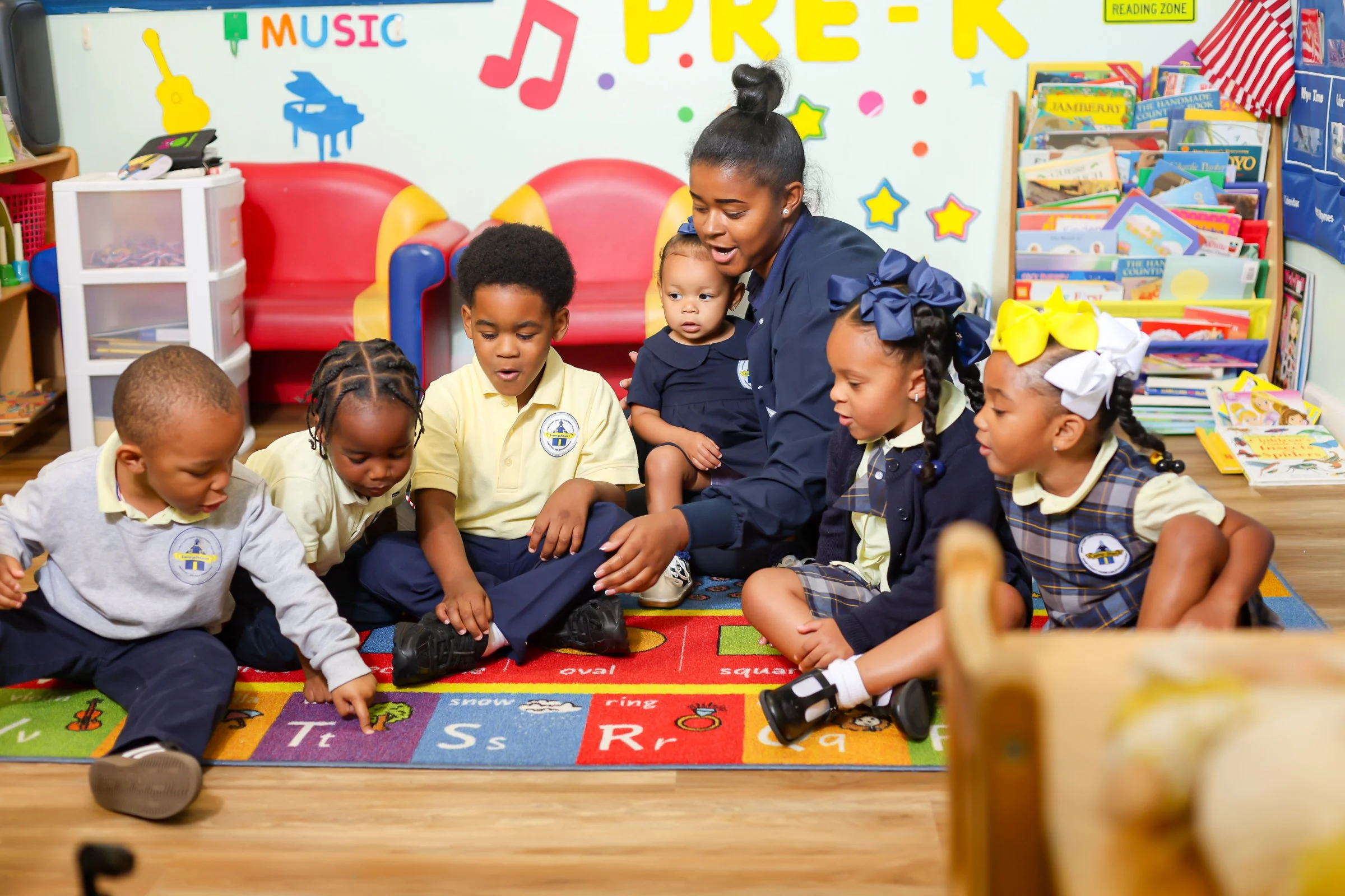 Students sitting with teacher on a rug reviewing the alphabet