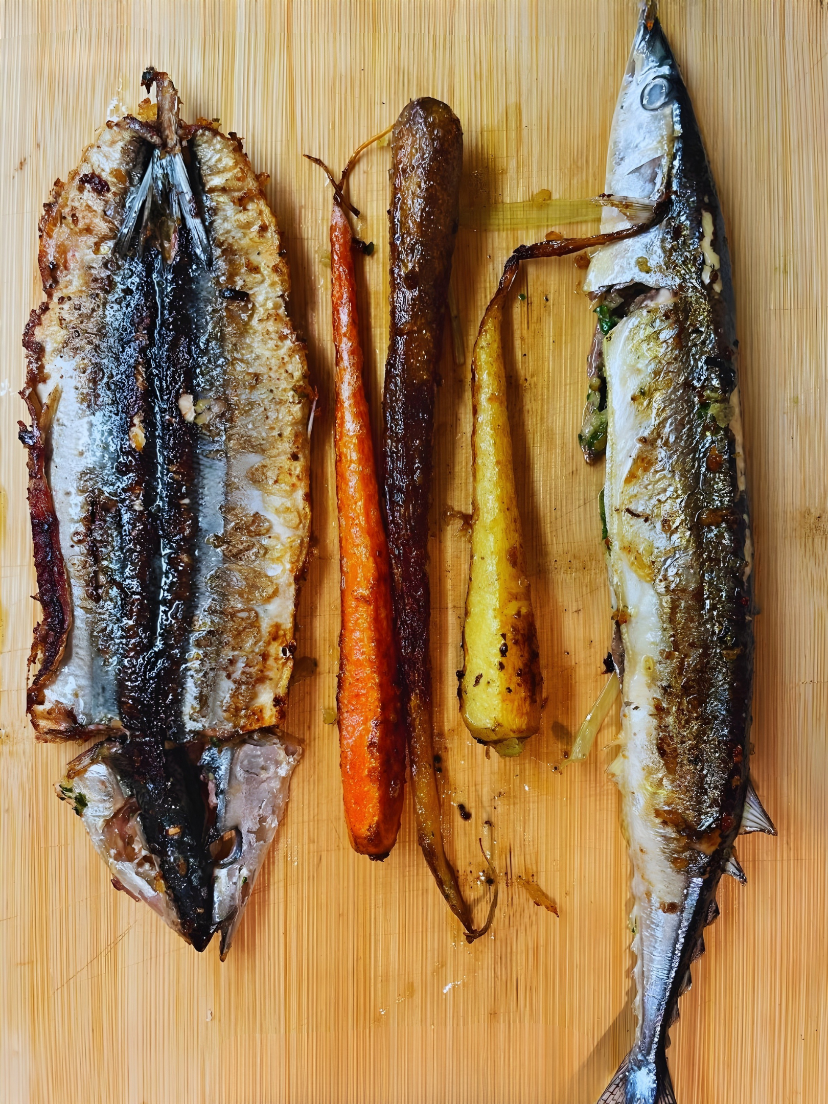 Overhead close up of grilled whole branzino with roasted carrots on a wooden board, showcasing Clementina’s celiac safe gluten free Italian seafood.