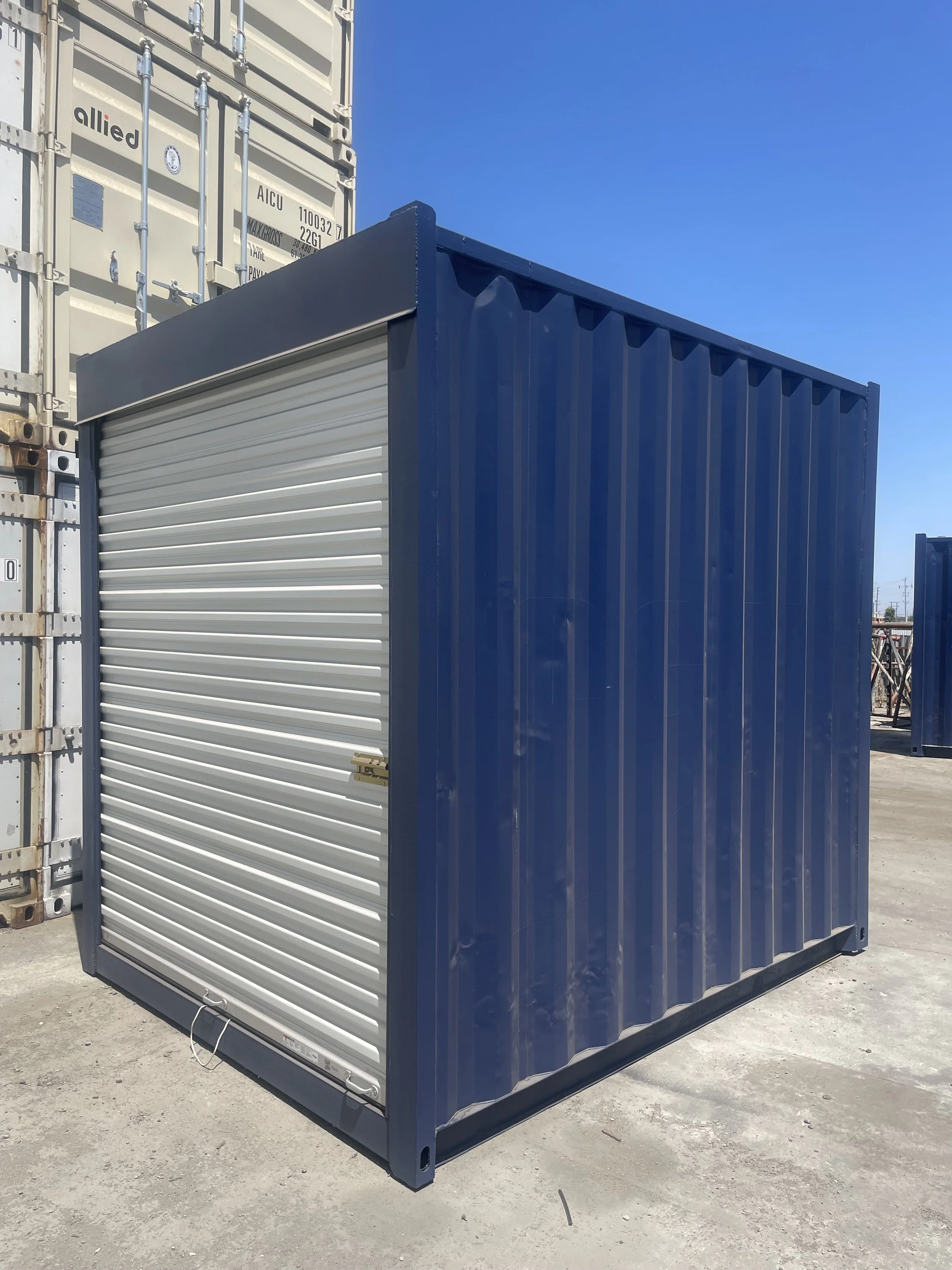 A small blue and gray storage container with a roll-up door, situated outdoors under clear blue sky.