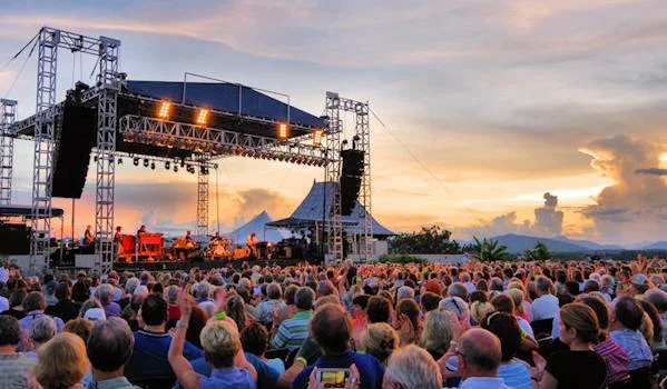 An outdoor concert at sunset with a large audience watching a stage with musical instruments.