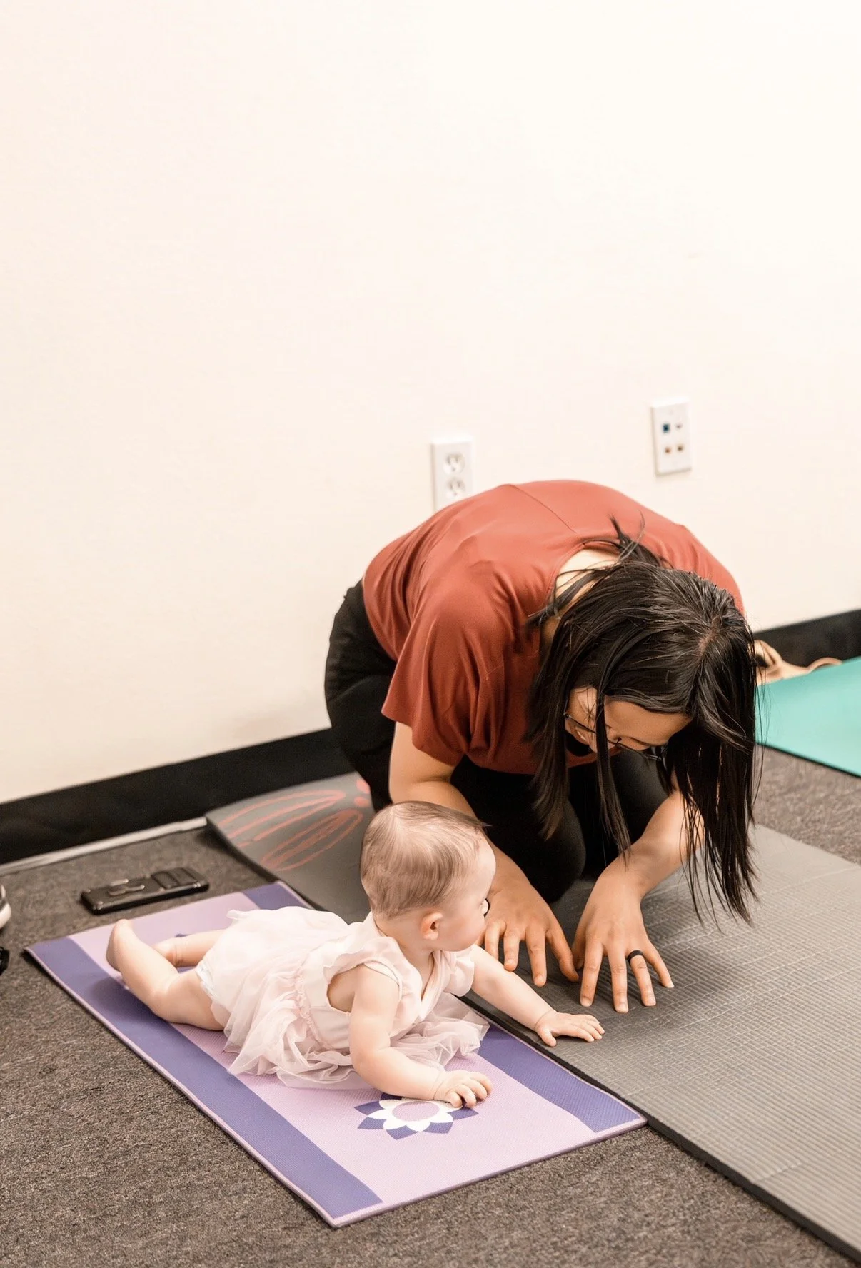 A woman helps a baby do a tummy time exercise on a yoga mat indoors.