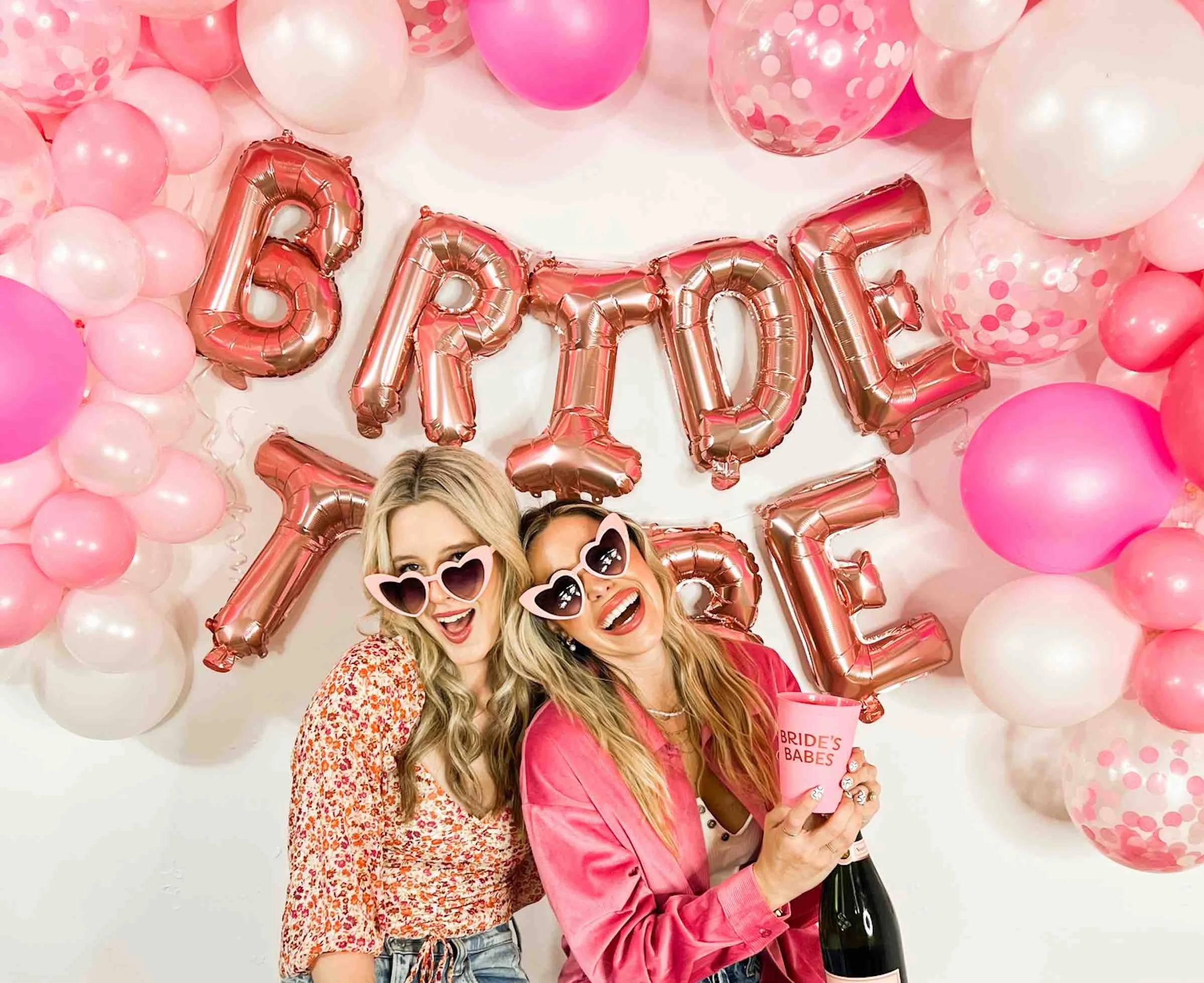 Two women in front of balloon backdrop with champagne