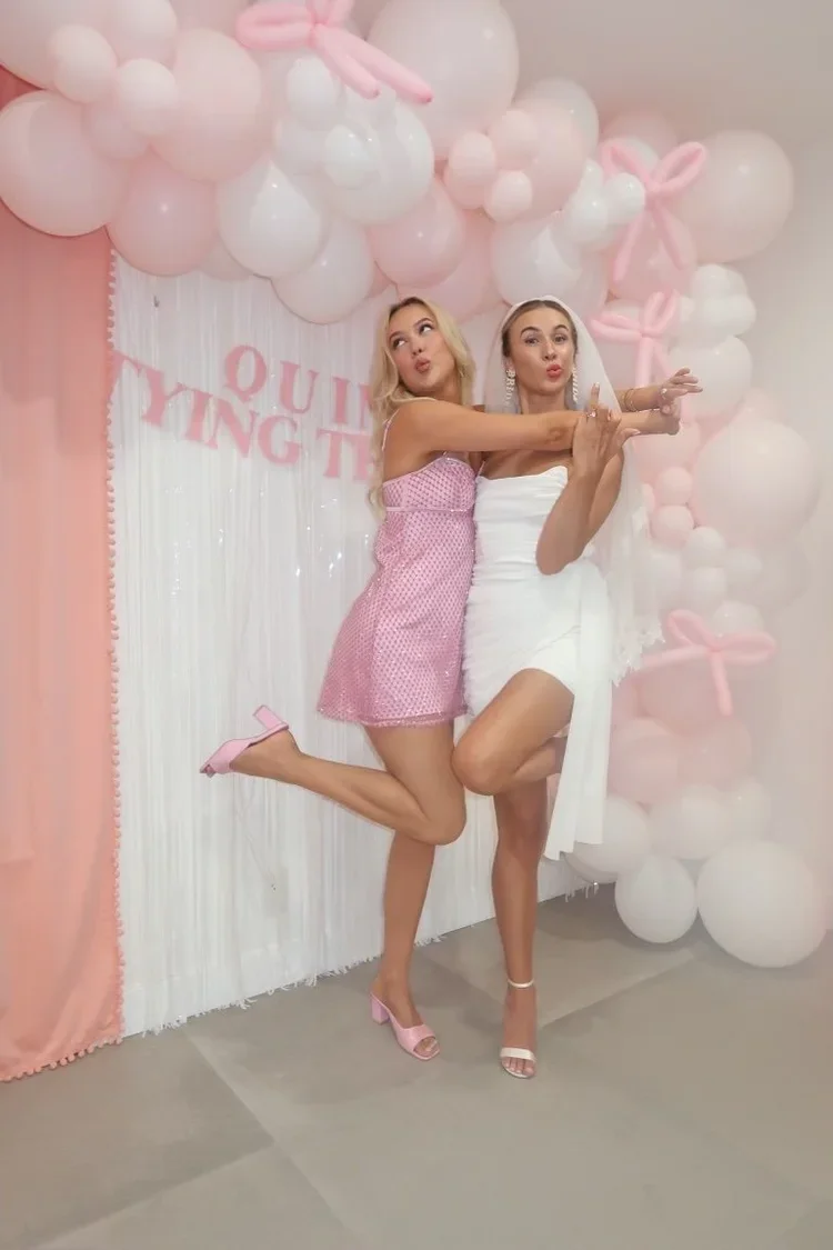 Two women posing in front of balloon backdrop