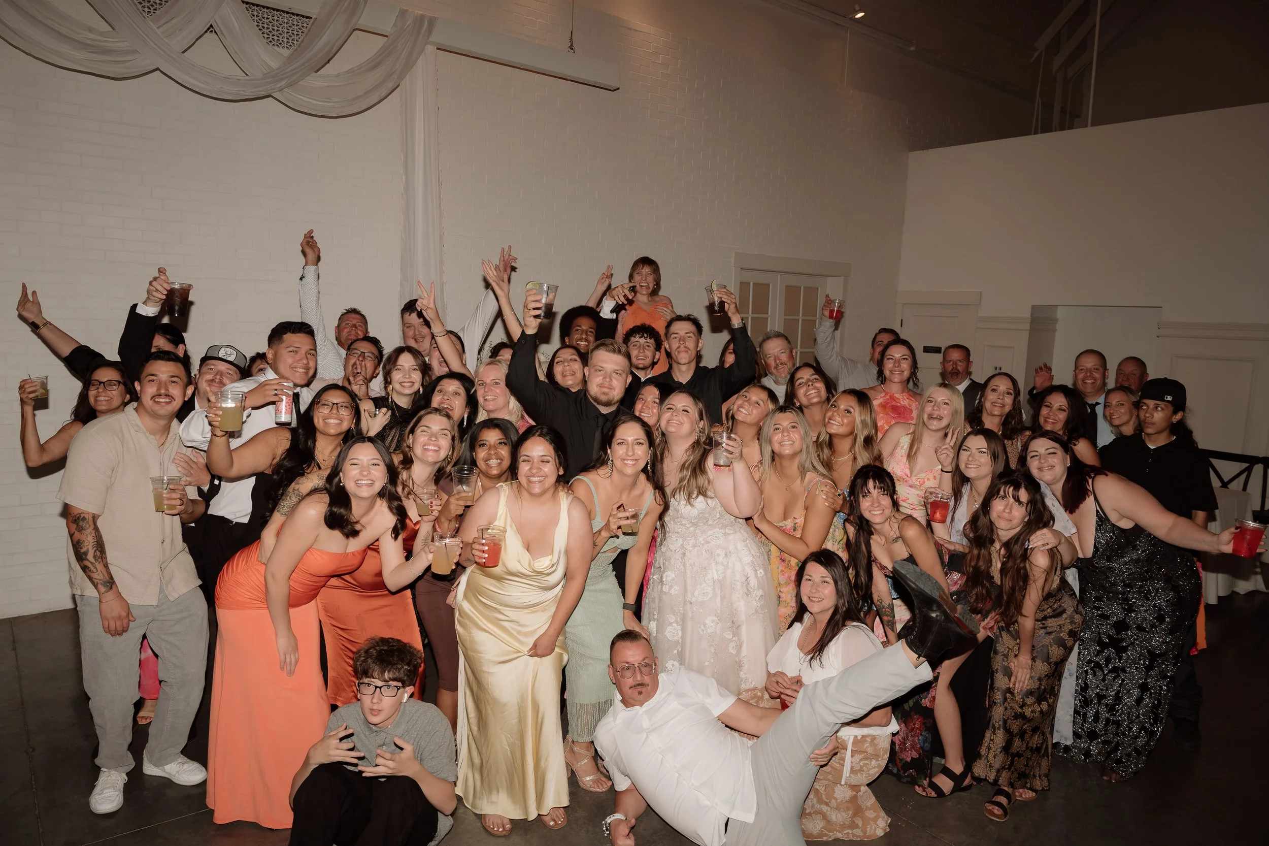 Large group of people celebrating at an indoor event, smiling, holding drinks, and posing for the camera.