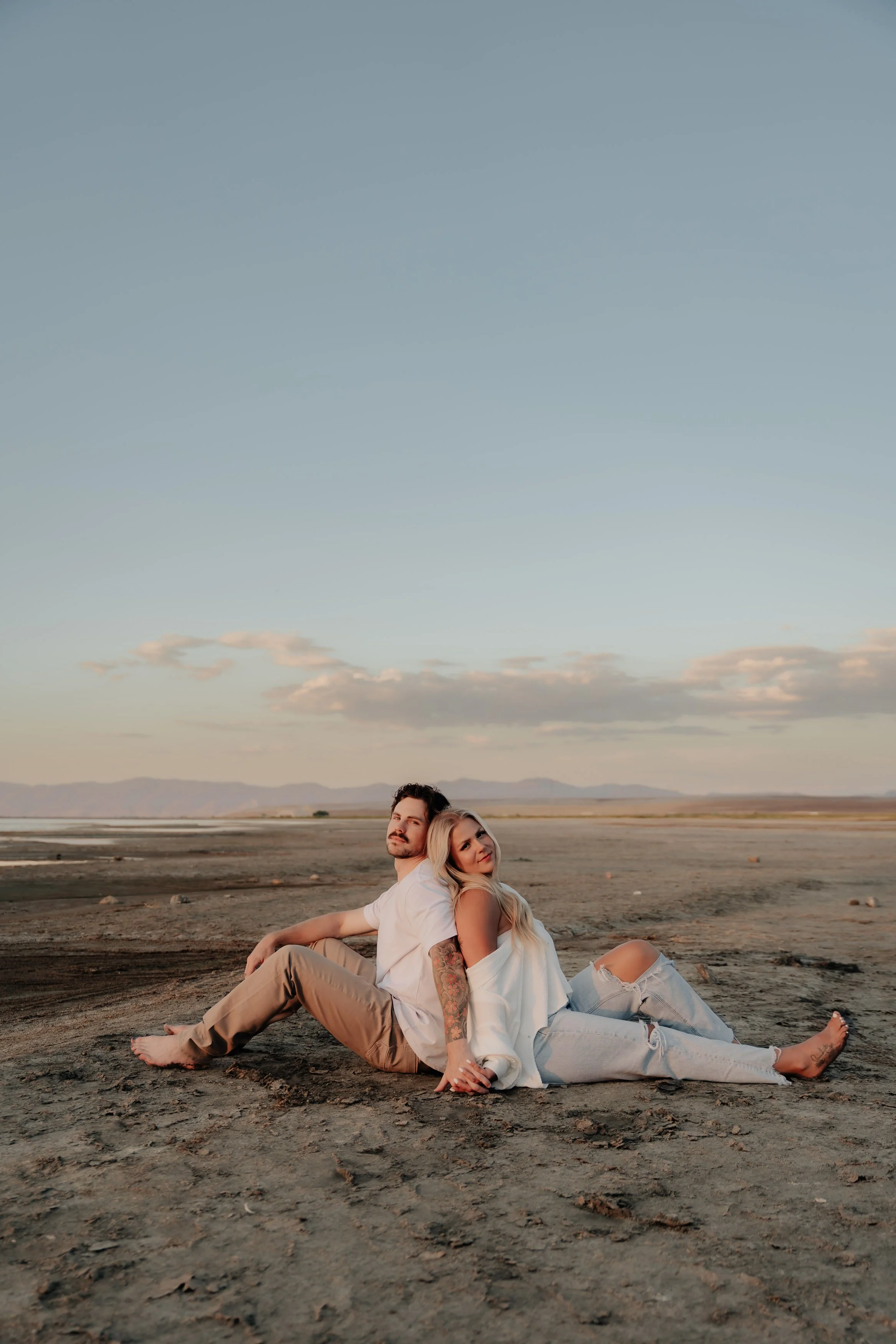 A couple sitting on the dry ground in a vast open landscape during sunset.