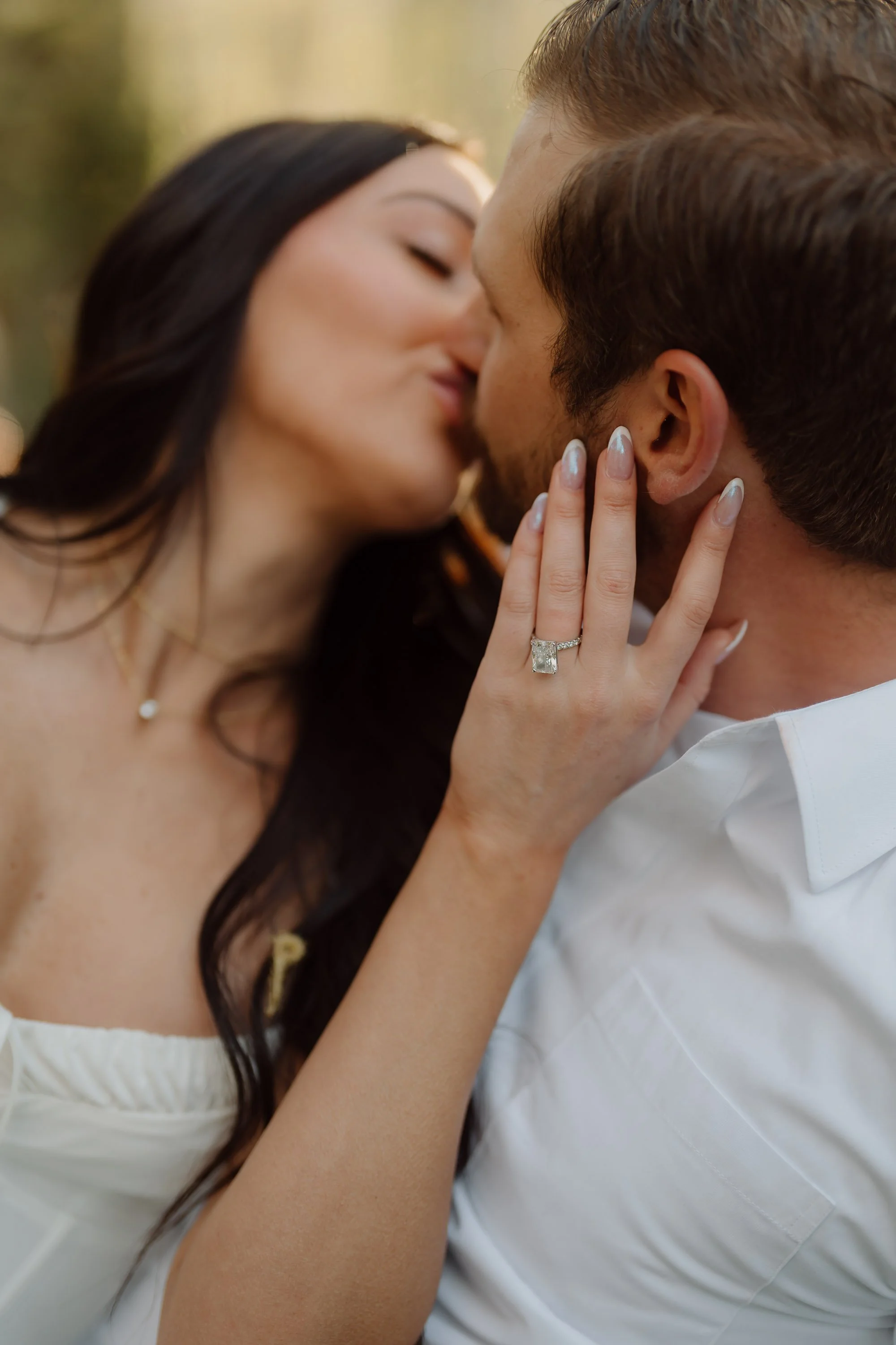 A couple sharing a kiss, with the woman touching the man's face and wearing an engagement ring.