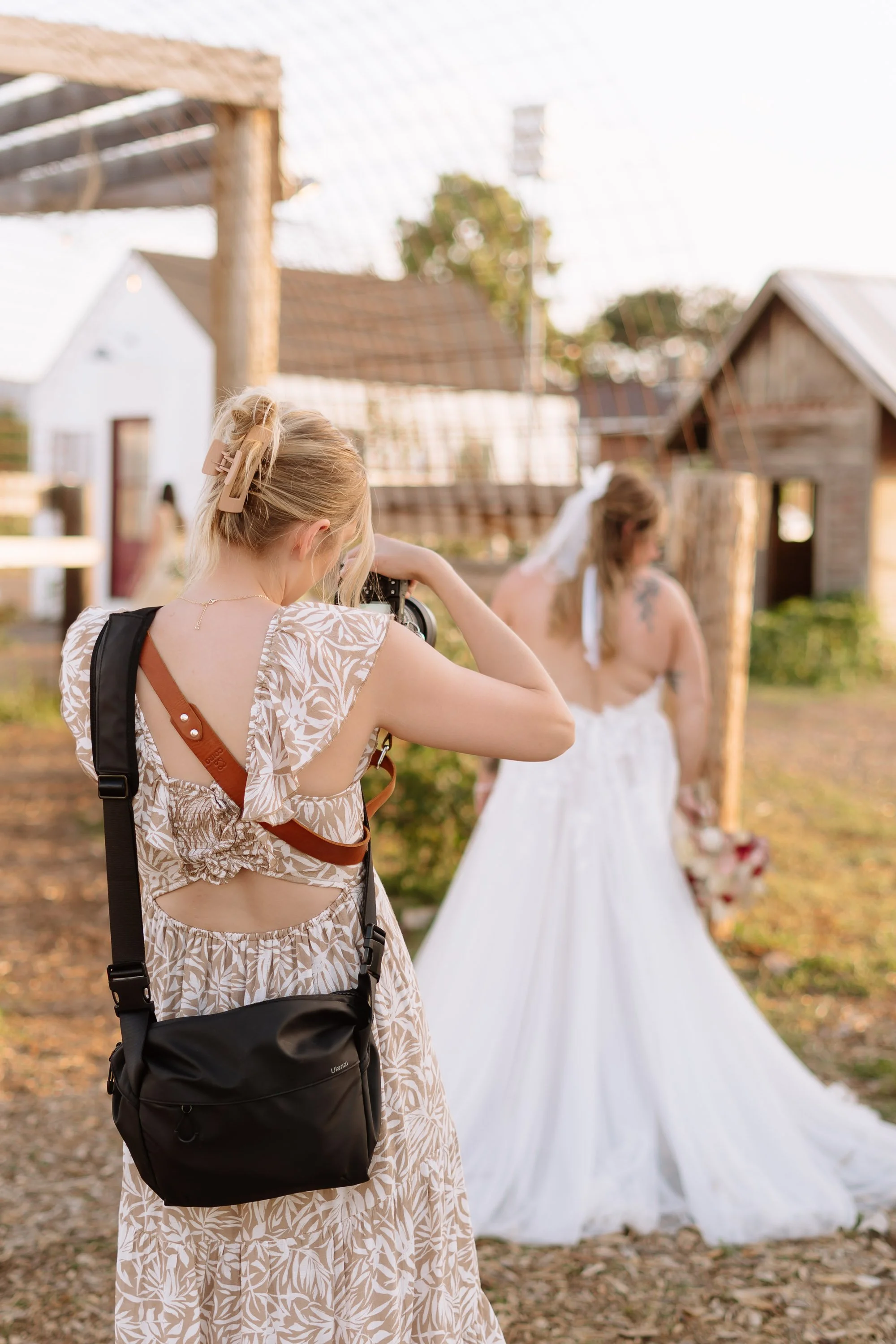 A photographer taking a picture of a bride holding a bouquet outdoors at a rustic farm setting.