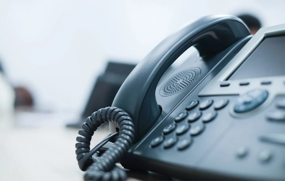 Close-up of a black office telephone on a desk with blurred background.