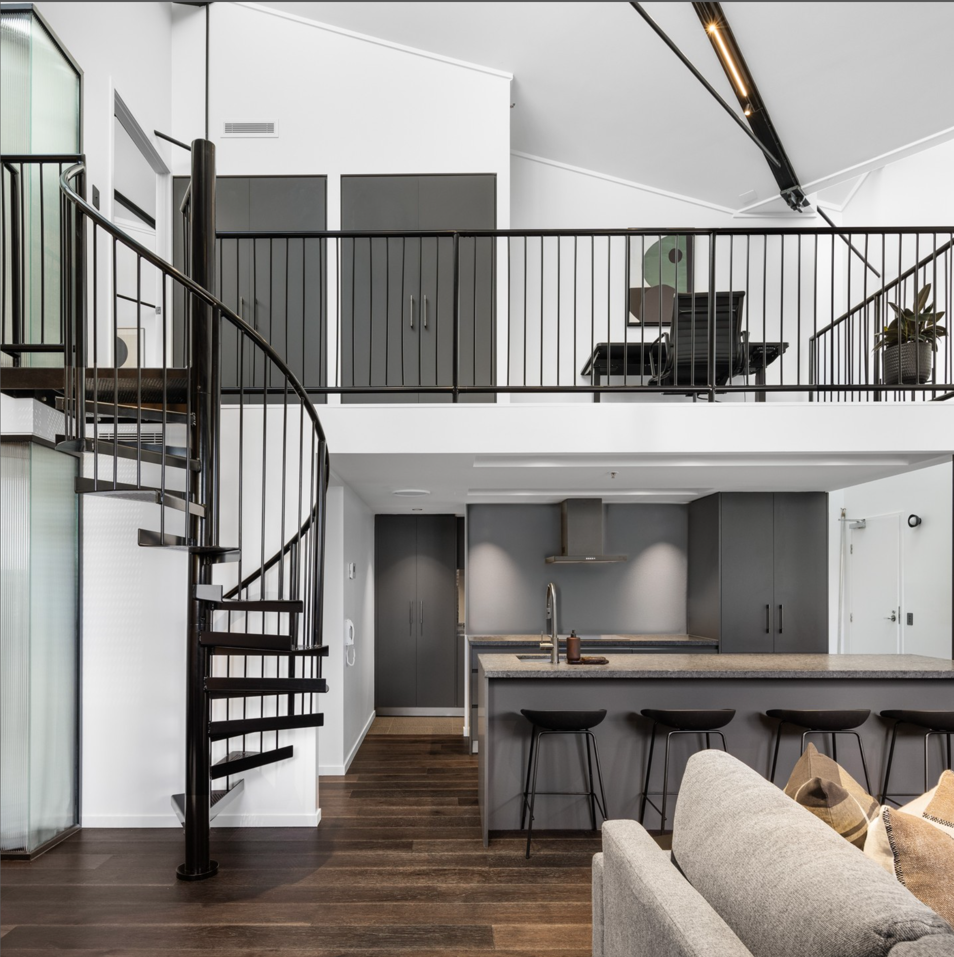 Modern two-story apartment interior with kitchen area on ground floor and loft on upper level, featuring gray cabinets, wooden floors, black staircase, and minimalist decor.