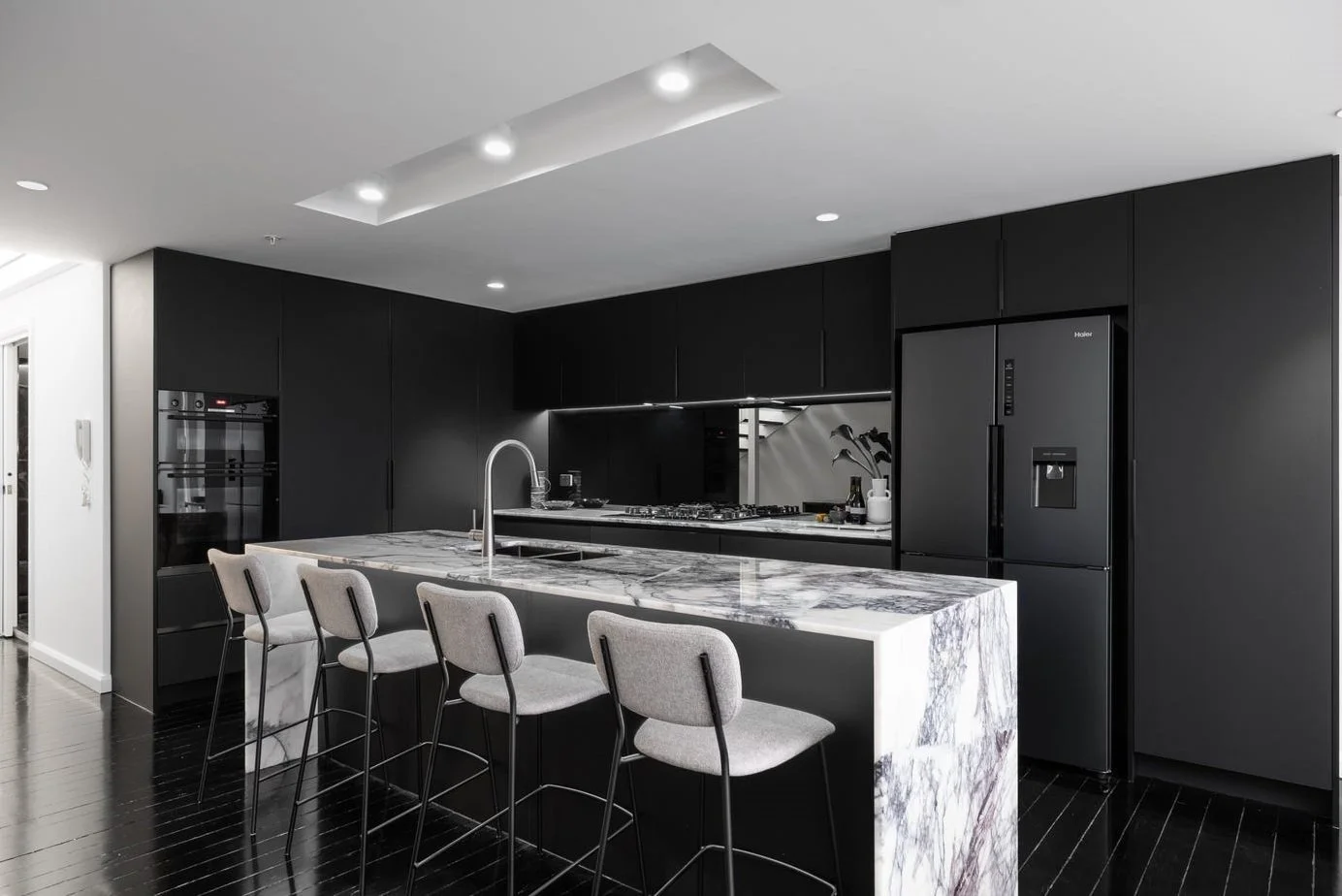 Modern kitchen with black cabinets, marble island, and gray bar stools.