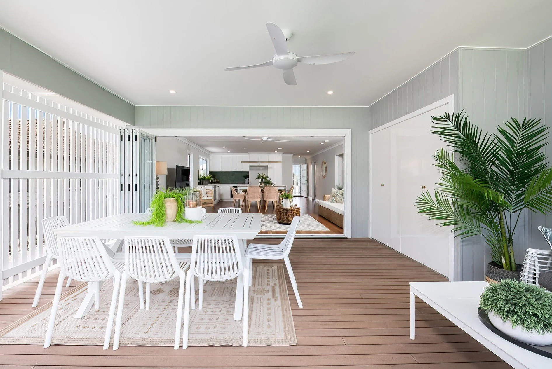 Exterior patio with white dining table and chairs, potted plants, and sliding glass doors leading to an indoor living space.