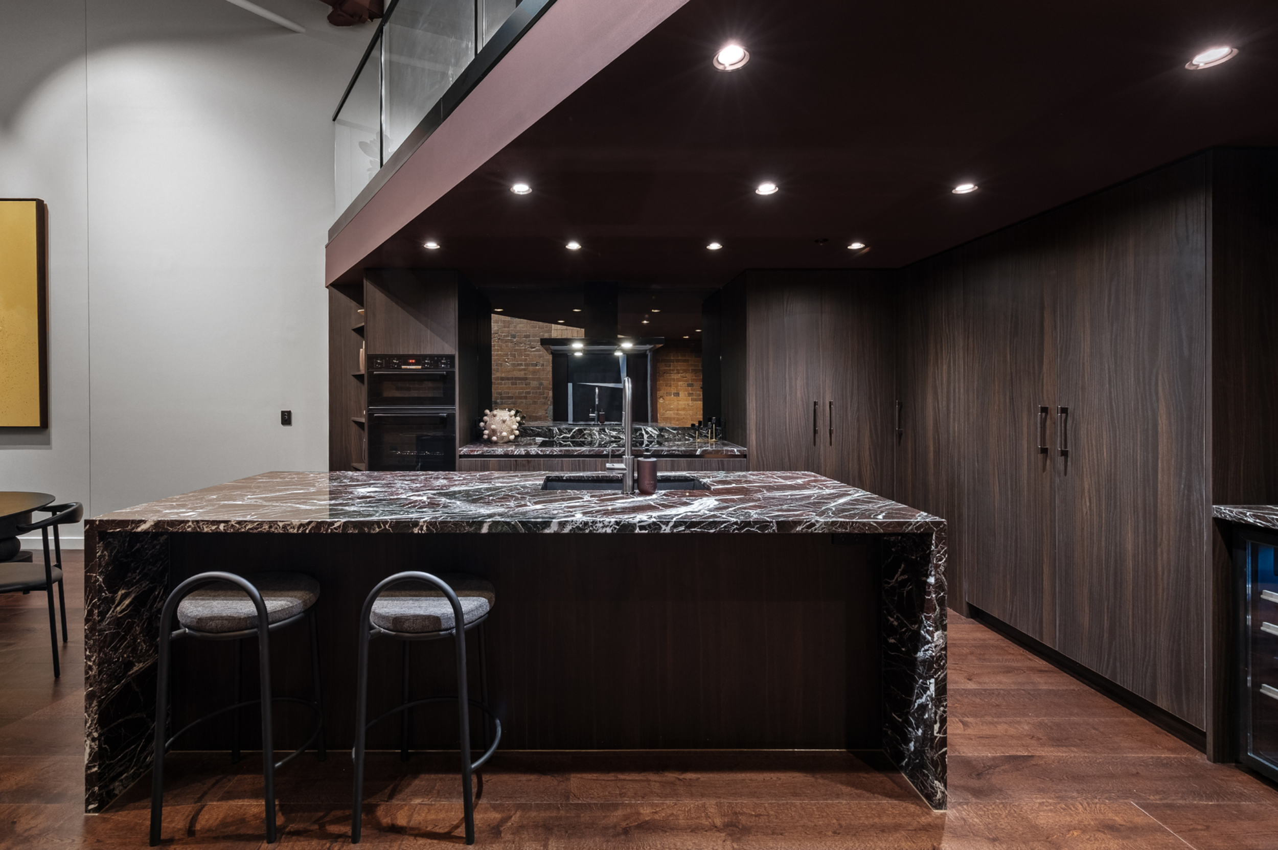Modern kitchen with a dark marble island, wooden cabinets, and recessed ceiling lights.