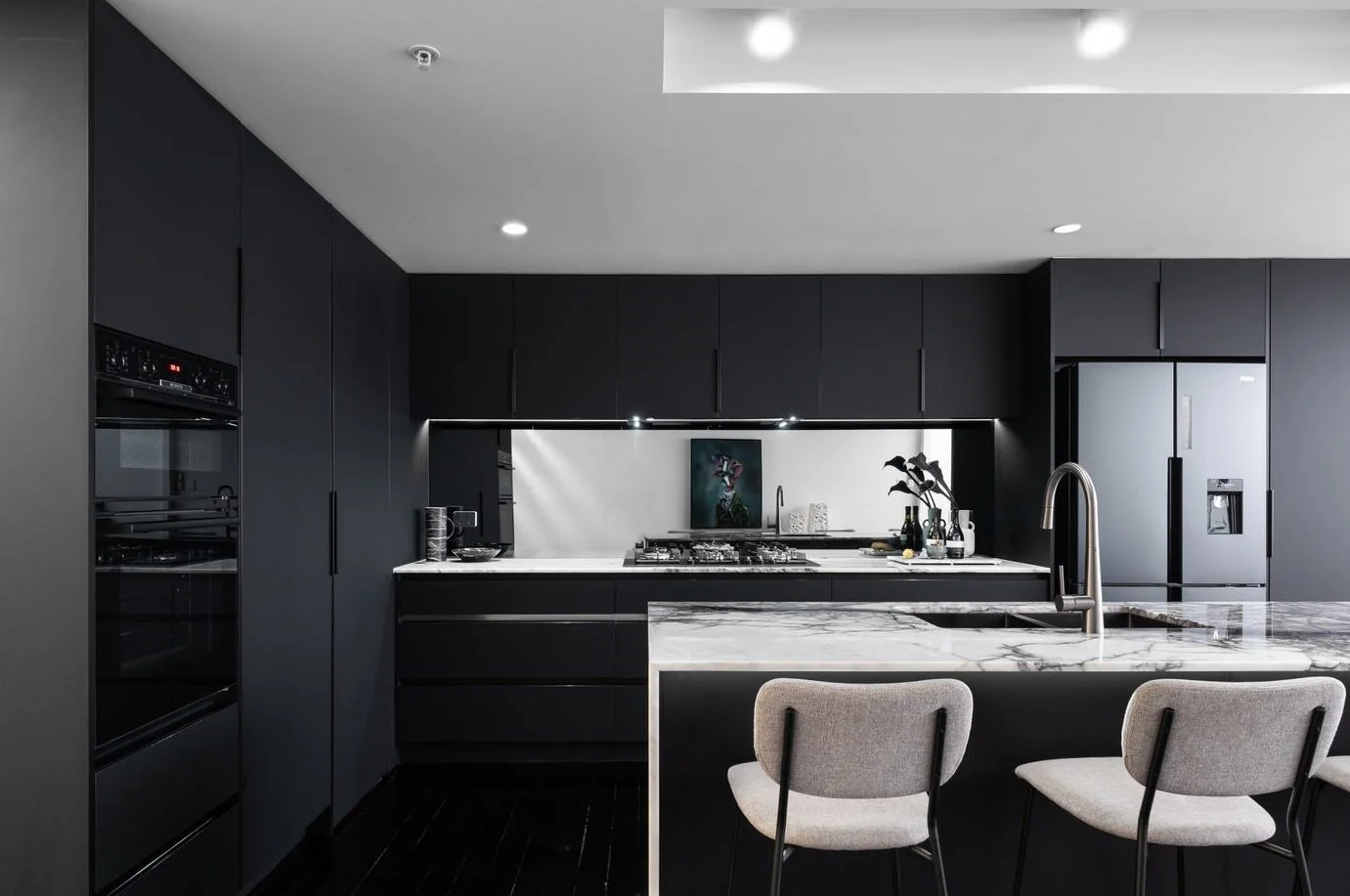 Modern kitchen with black cabinetry, white marble countertops, a central island with bar stools, stainless steel appliances, and a sink with a high-arc faucet.