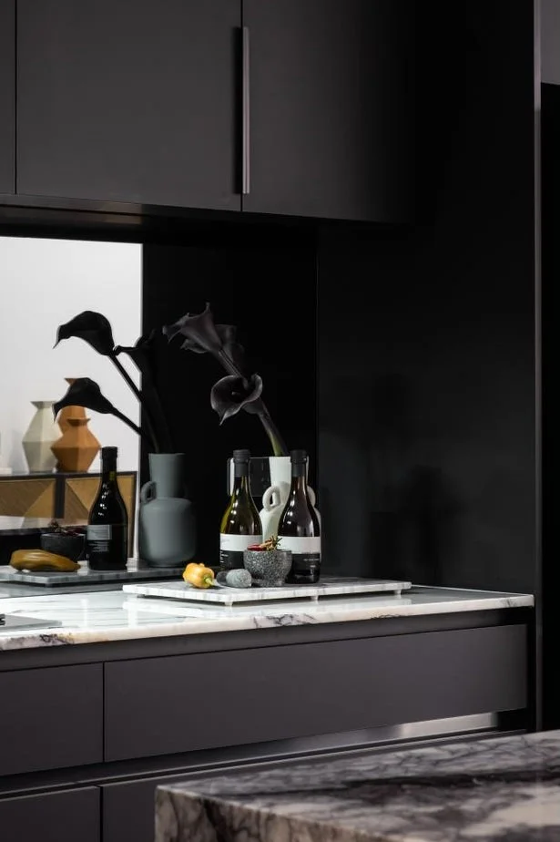 A modern kitchen with a dark color scheme featuring black cabinets, a marble countertop, and decorative bottles and vases.
