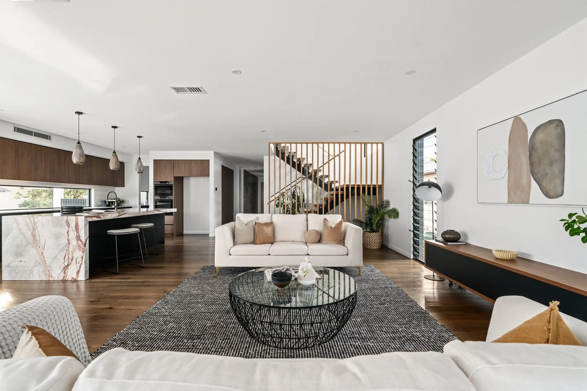 Modern open-plan living room with white sofas, black wire coffee table, wooden flooring, and wall art with abstract shapes