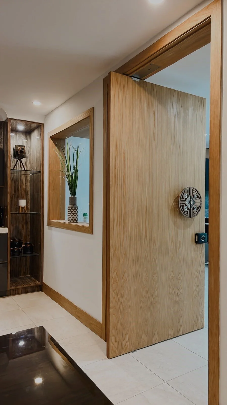 Wooden door partly open in a modern interior with a decorative wall piece, a framed mirror, and a display shelf with decor and a camera statue.