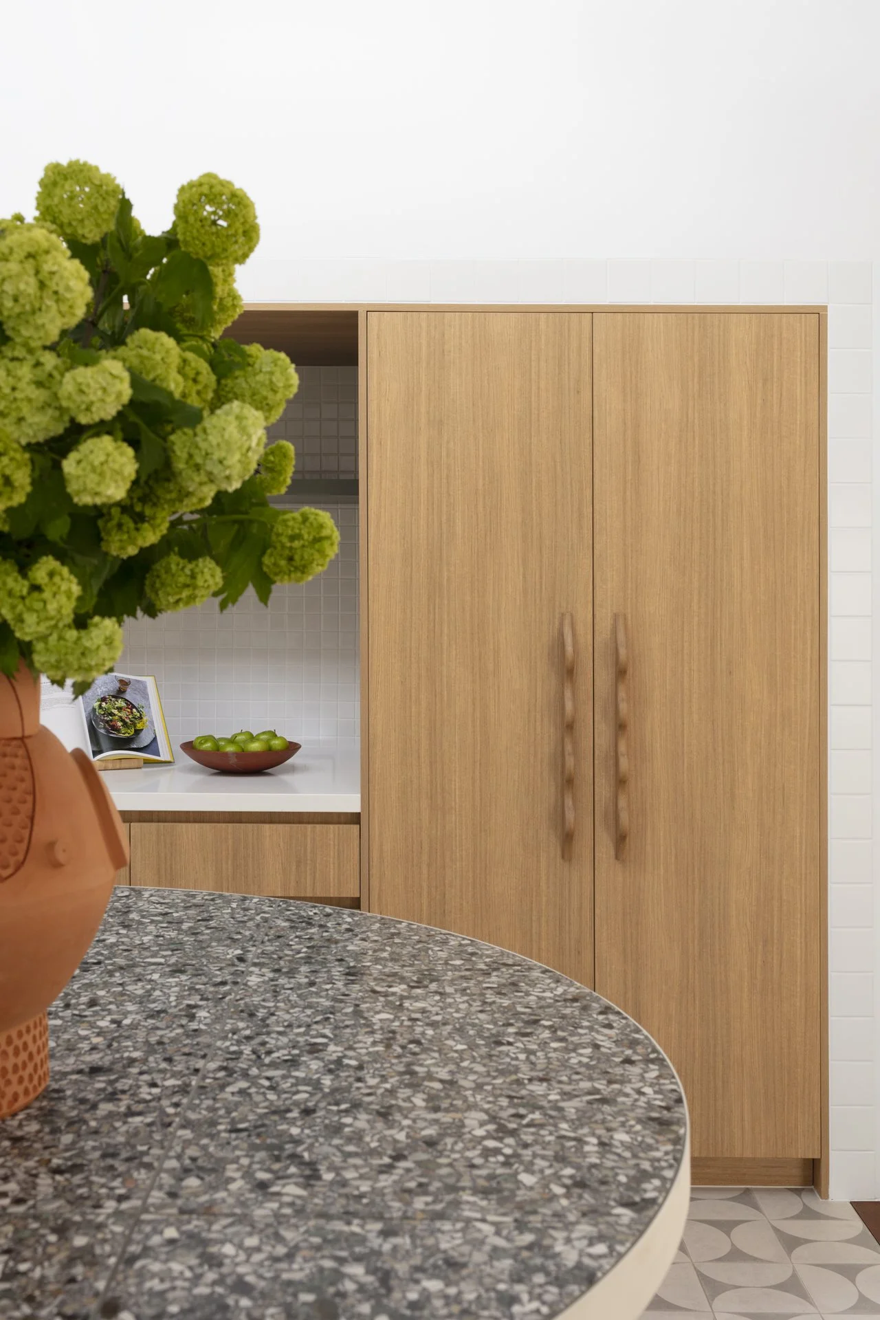 A kitchen with a speckled gray and black countertop, a vase with green flowers, and a wooden cabinet with closed doors.
